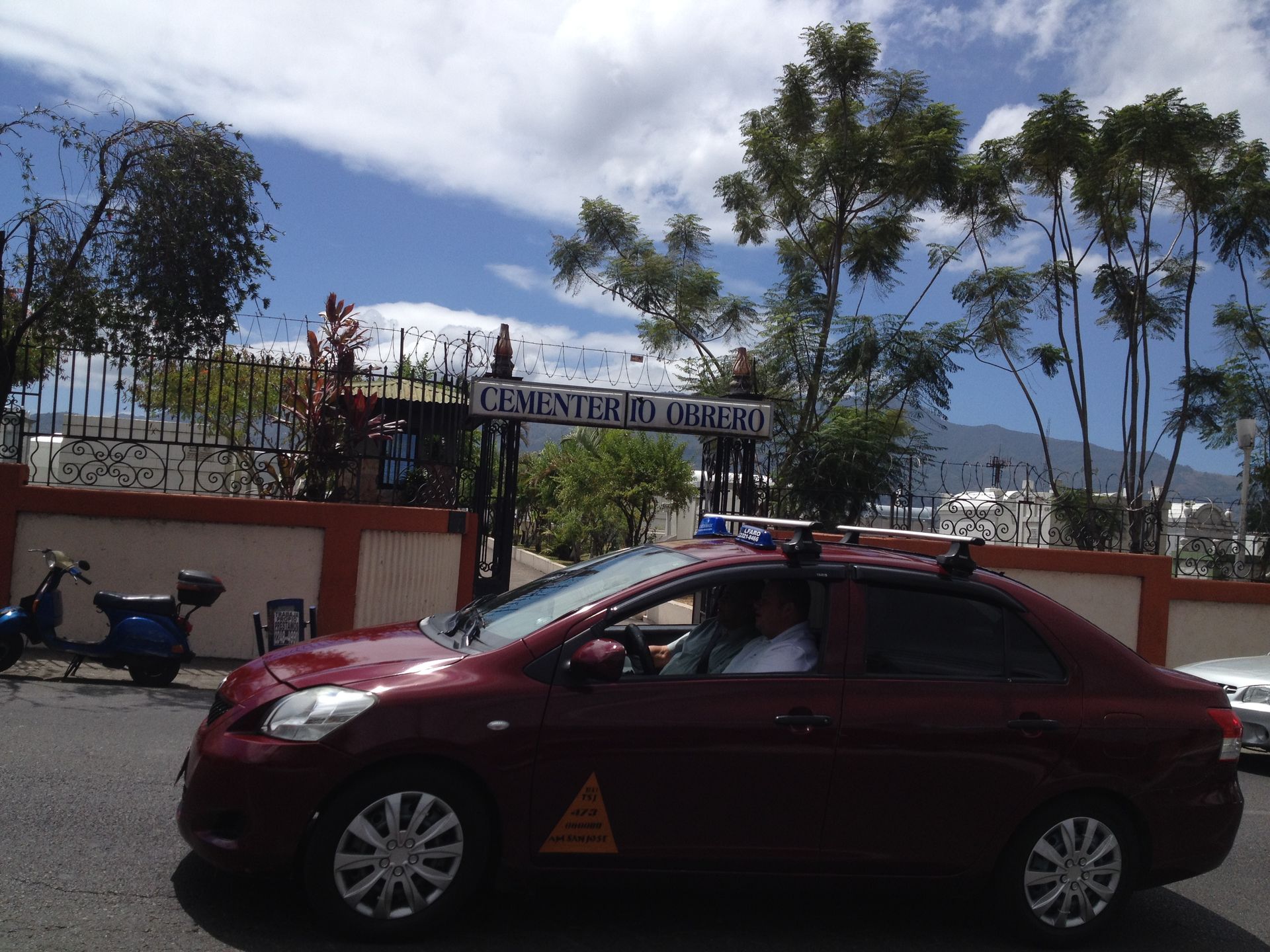 Red sedan with emergency lights drives past a gate with a sign that reads 
