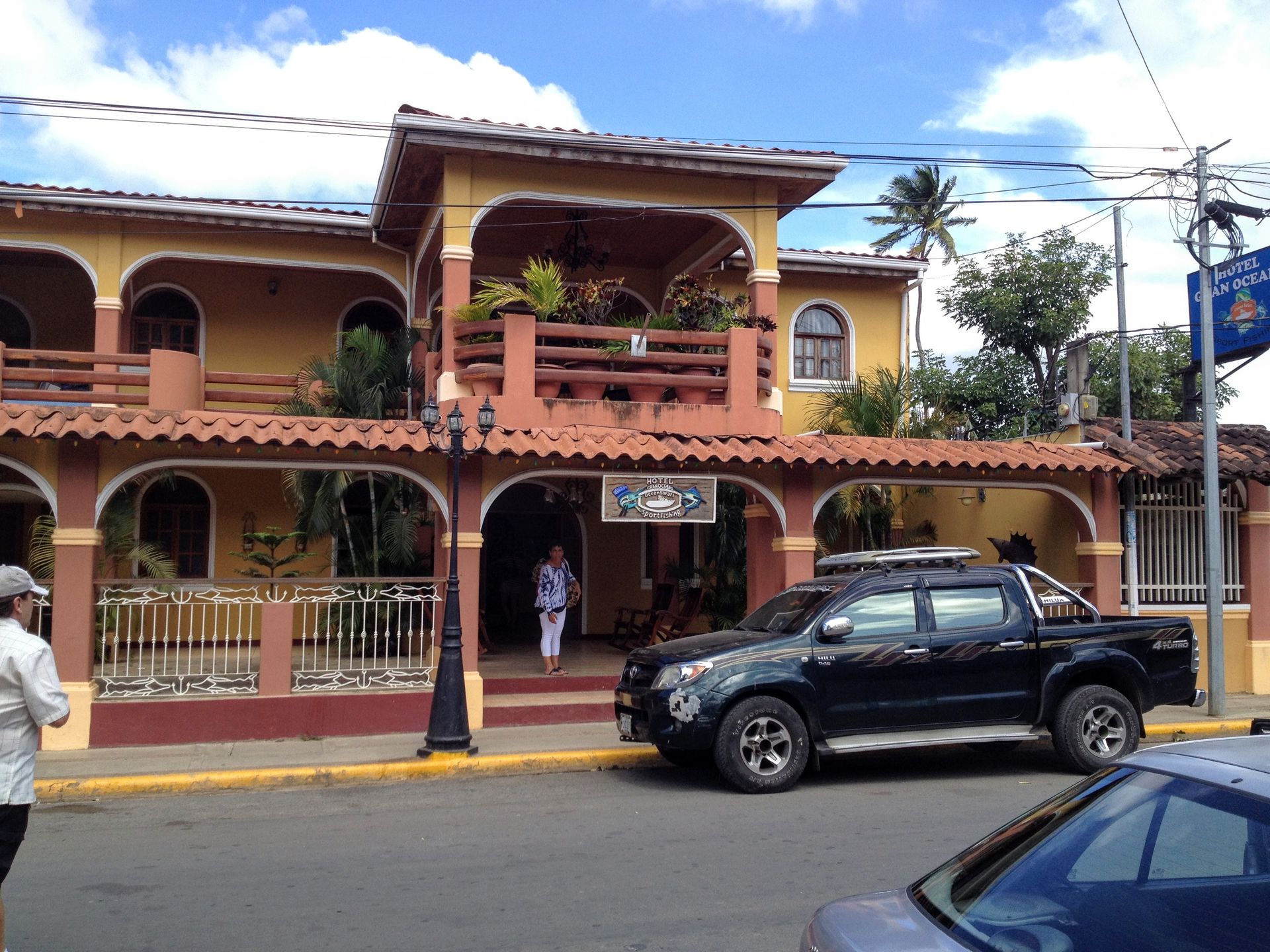 Yellow building with red tile roof, black pickup truck parked in front. Person entering building.