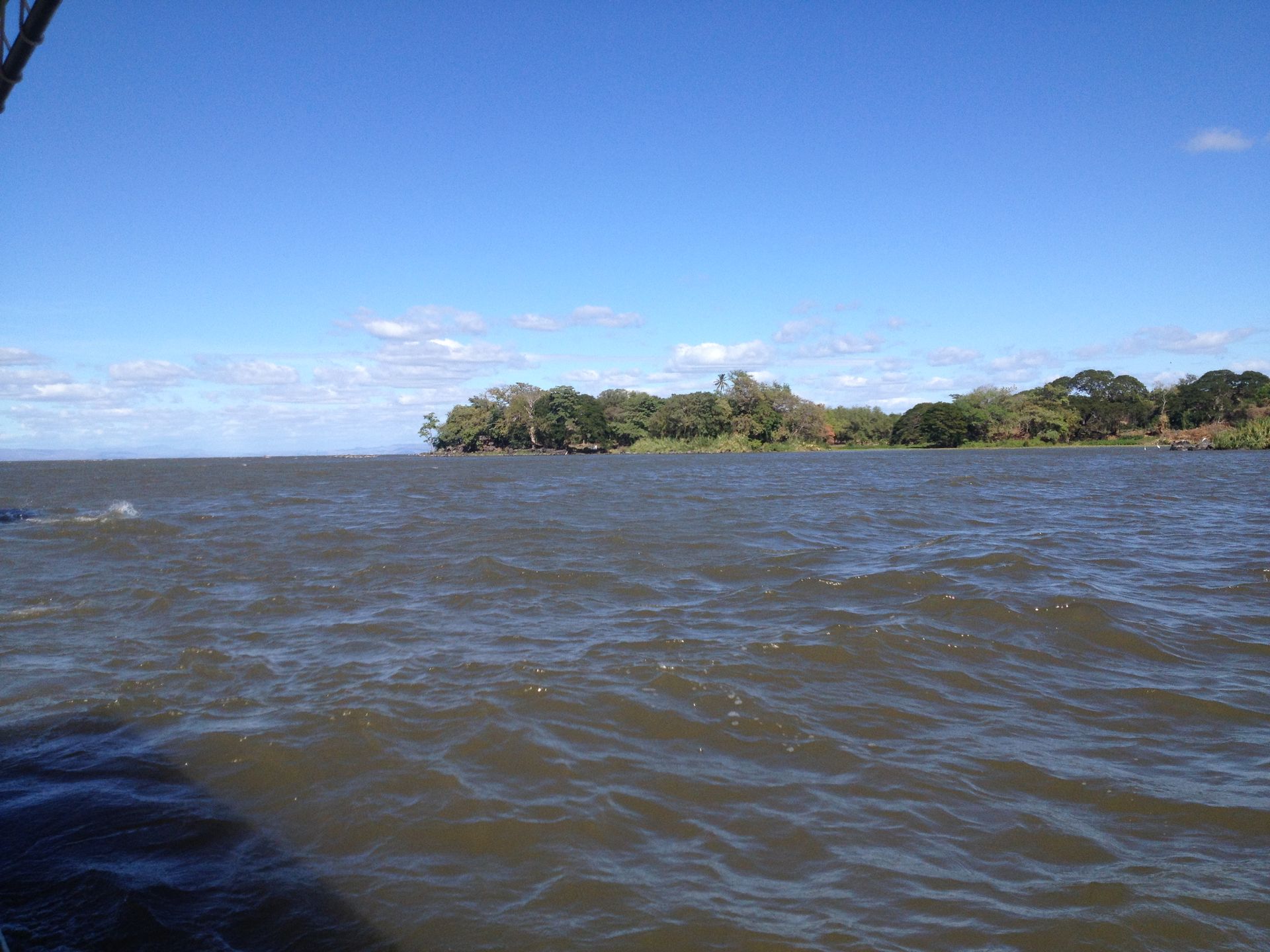 View of a large body of water, with an island covered in trees under a clear, blue sky.
