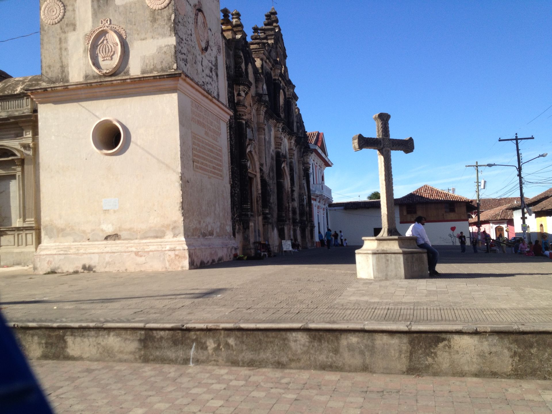 Stone cross in plaza, next to a church with ornate facade. Clear, sunny day.