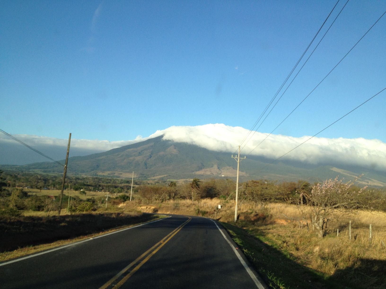 Road leading to a mountain partially covered in clouds under a blue sky.