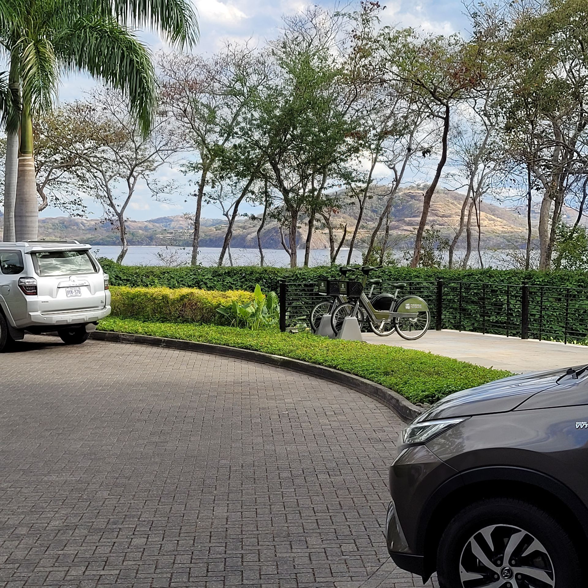 Vehicles parked near a walkway with a scenic view of water and hills.
