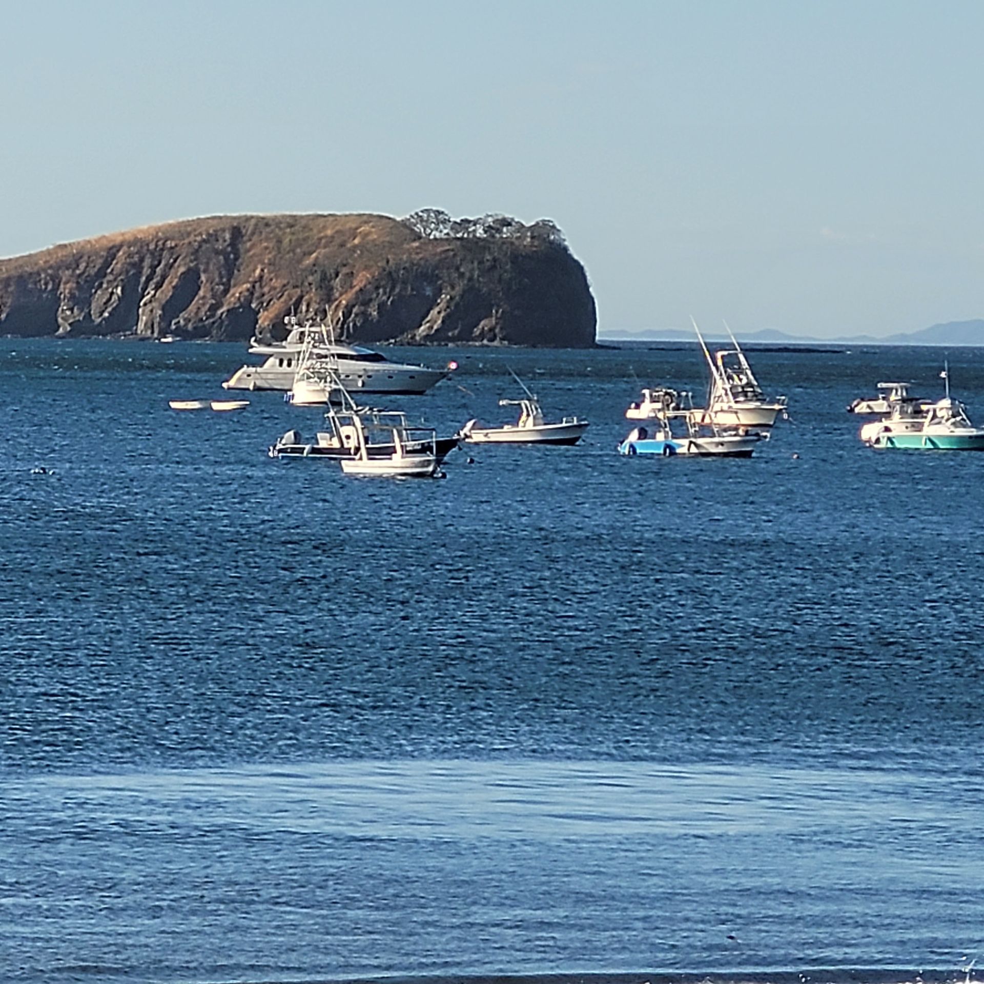 Boats on blue water, a rocky island in background, bright sunny day.