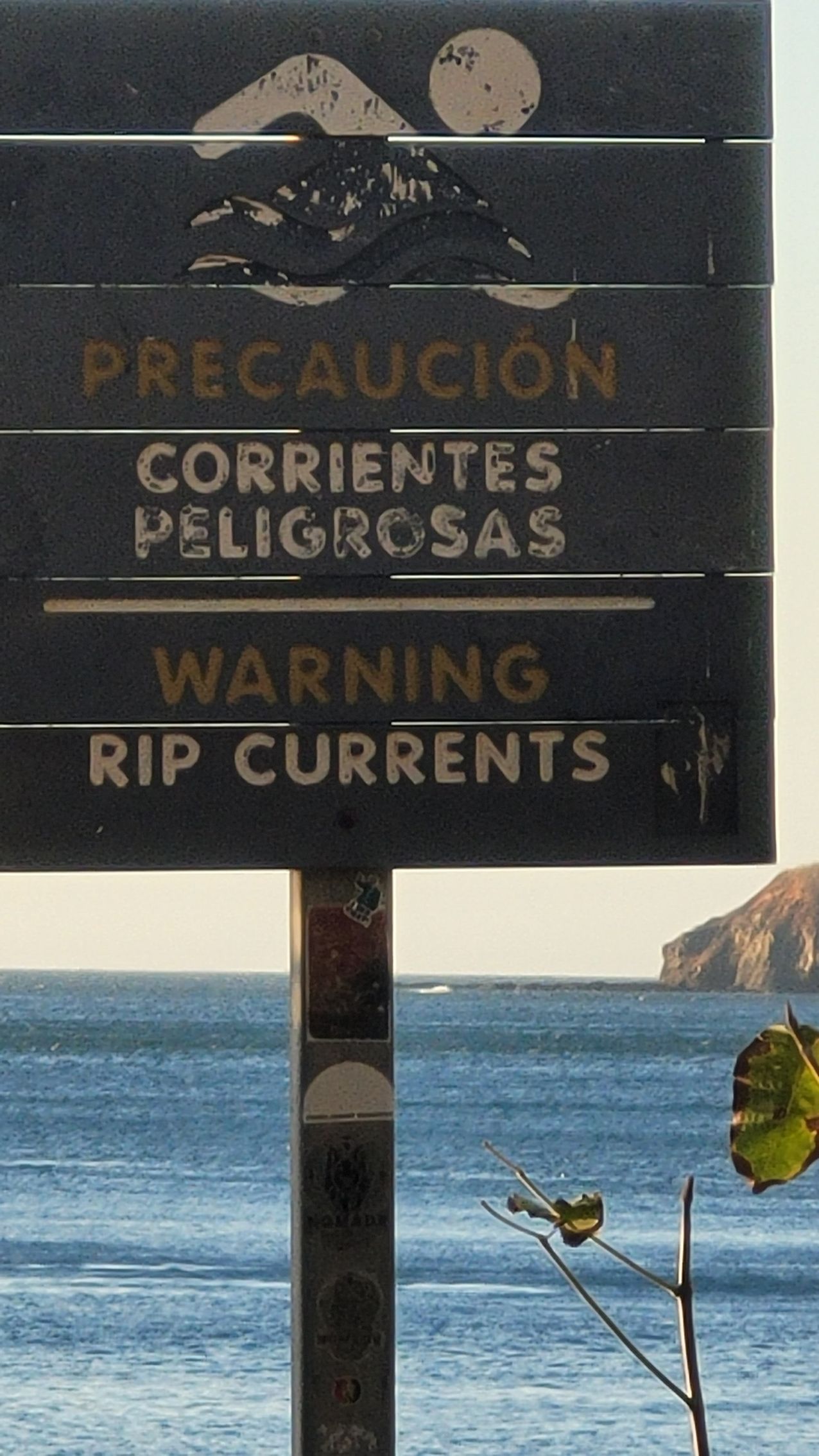 Sign warning of rip currents in Spanish and English at a beach.