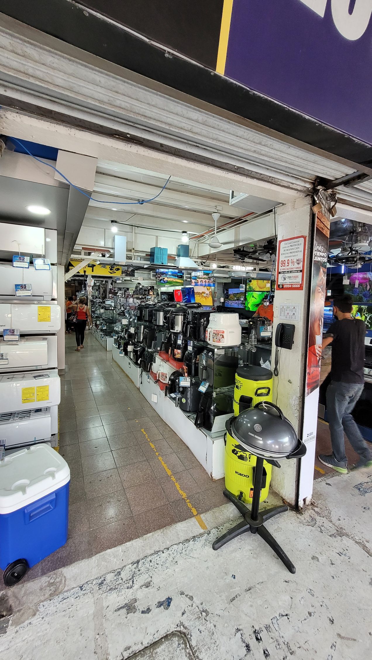 Exterior of a shop filled with various items, including coolers, equipment, and a grill. A person is visible.