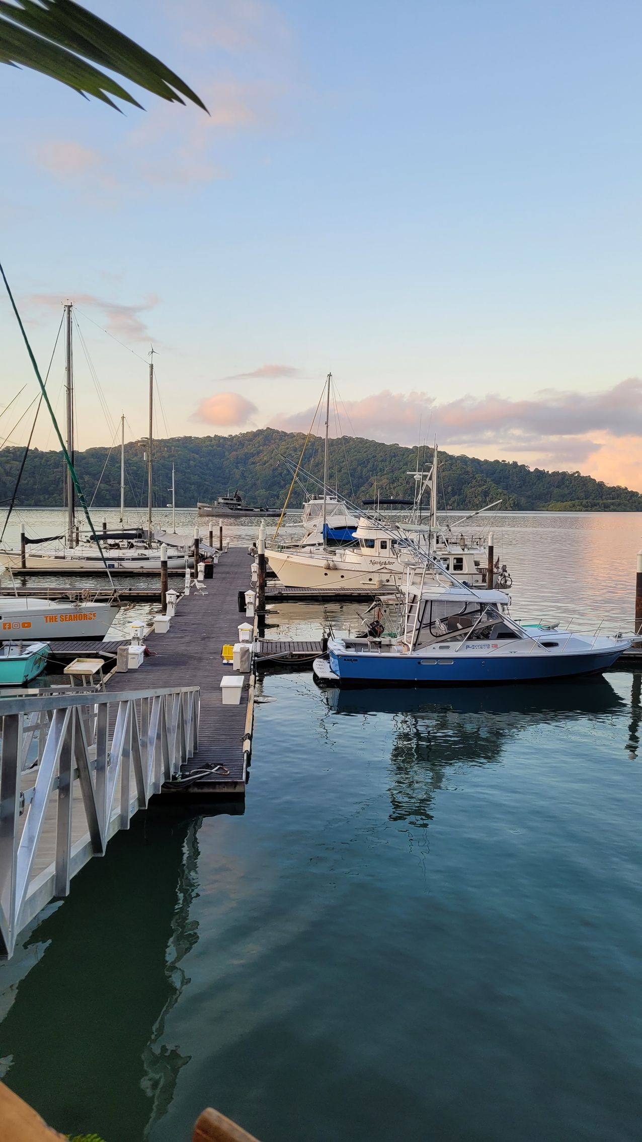 Boats docked at a pier at sunset; water, sky, and hills in the background.