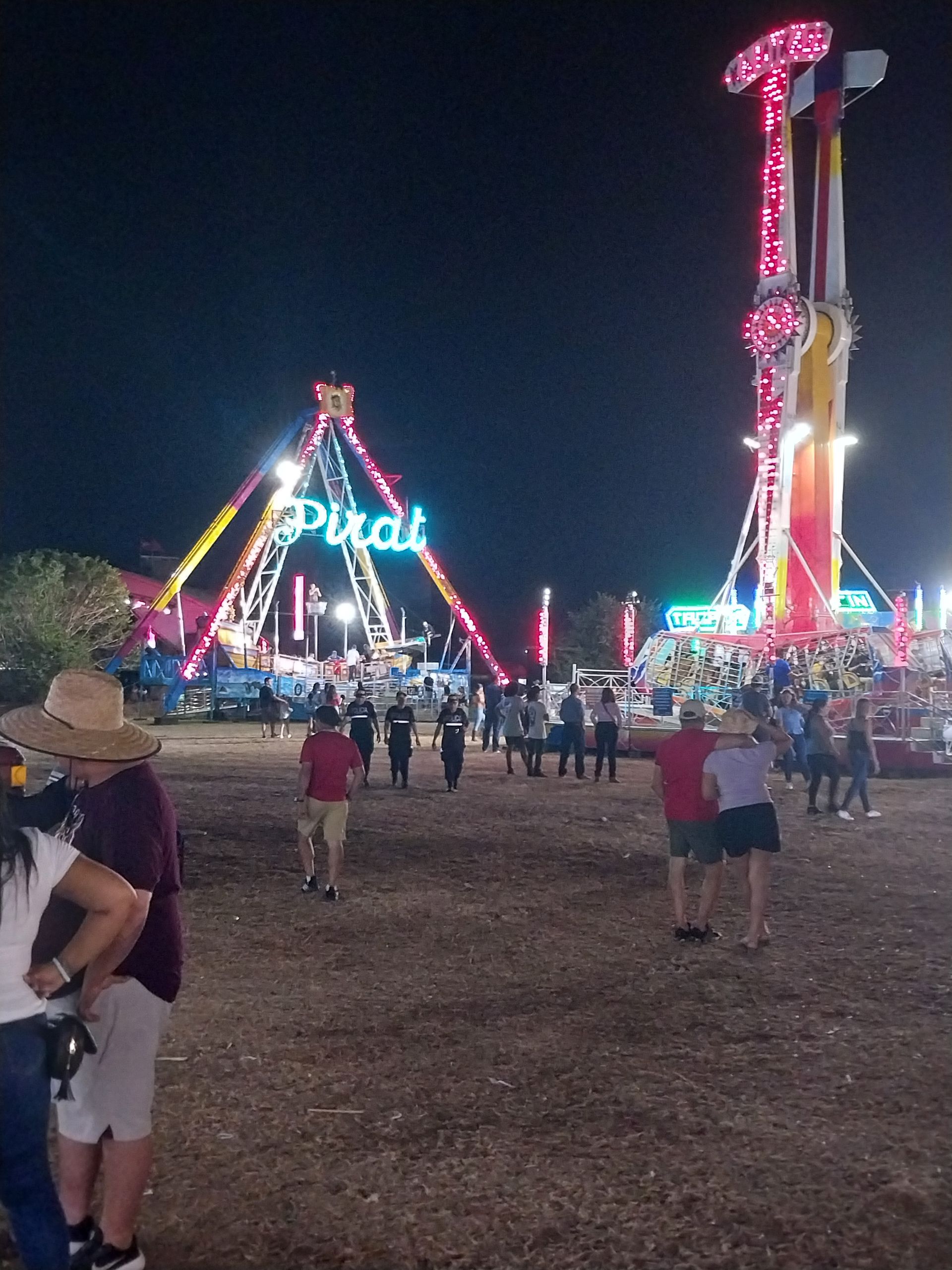 Nighttime carnival scene with illuminated rides, crowd of people gathered.