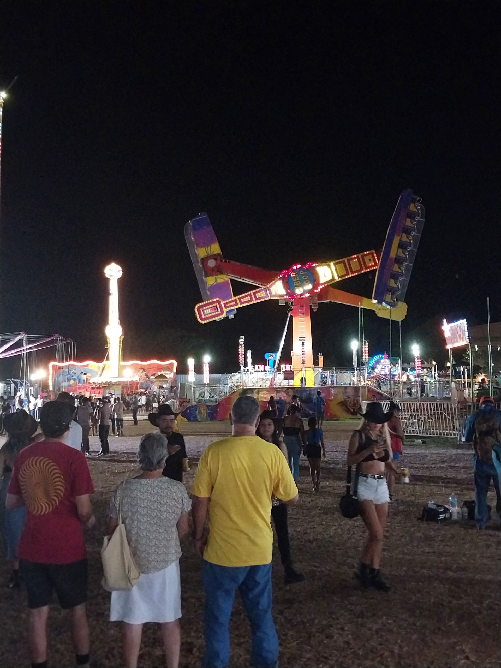 Fairground at night with amusement rides and people.