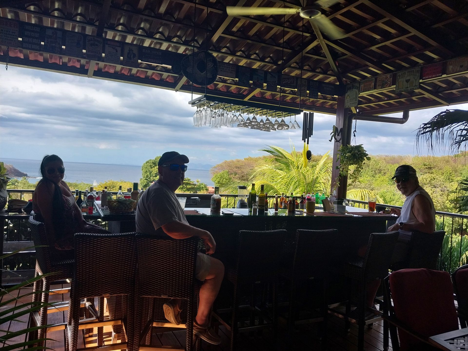 People at an open-air bar overlooking the ocean under a wooden roof.