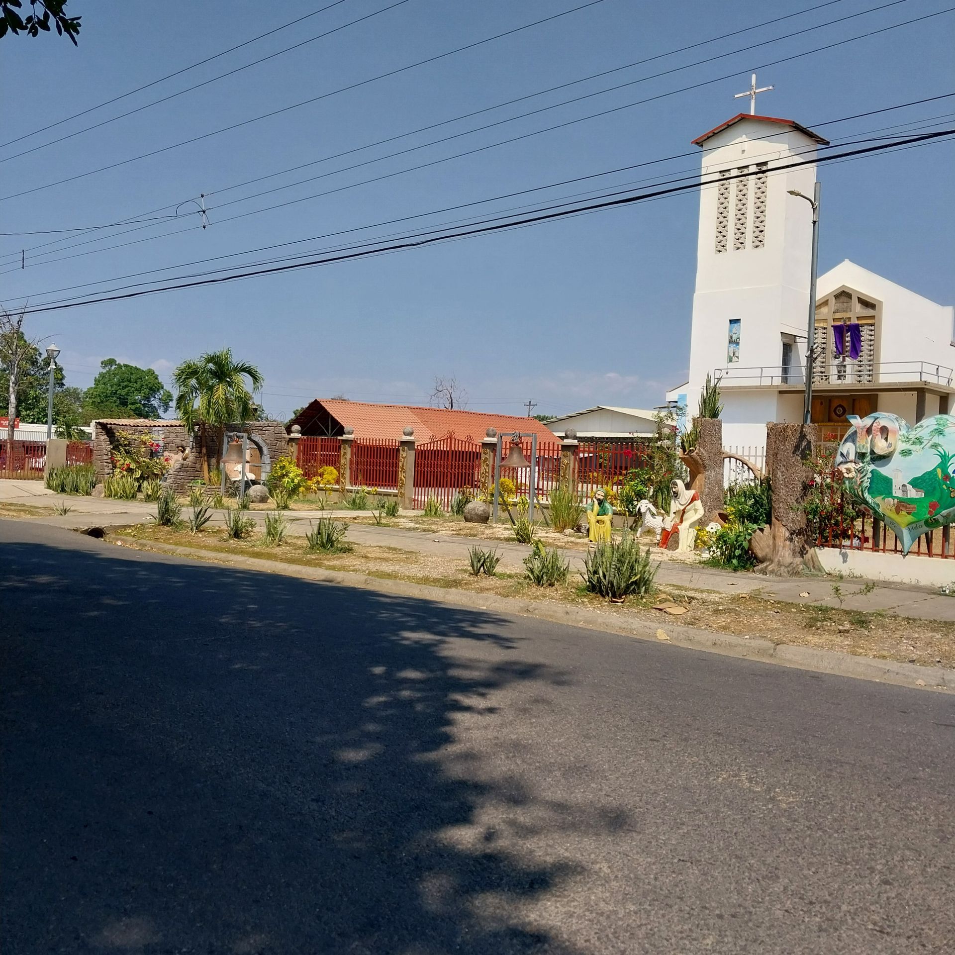 White church with a cross on top, adjacent building with red roof, and green trees.