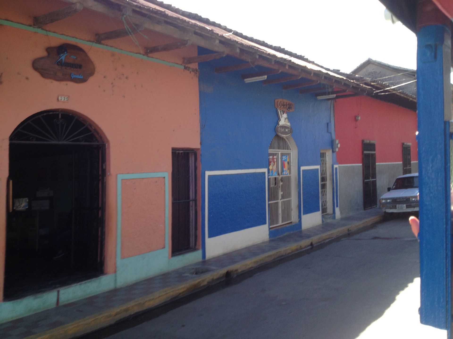 Colorful buildings line a street. A pink building is next to a blue building. A car is visible.