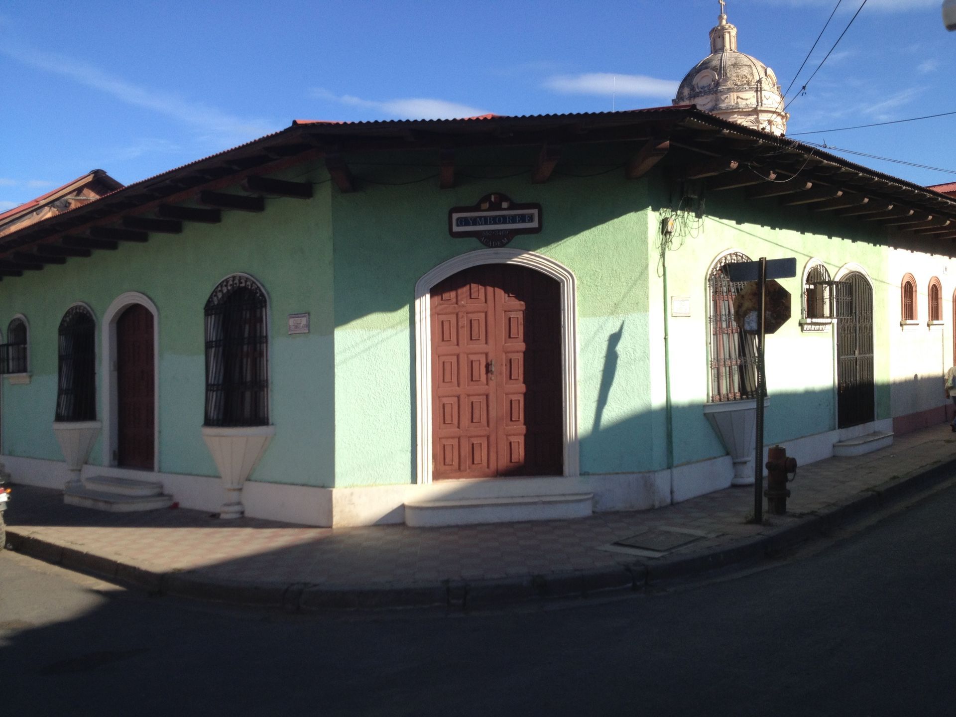 Corner building, light green walls, brown doors, tiled roof, dome in background, daytime.