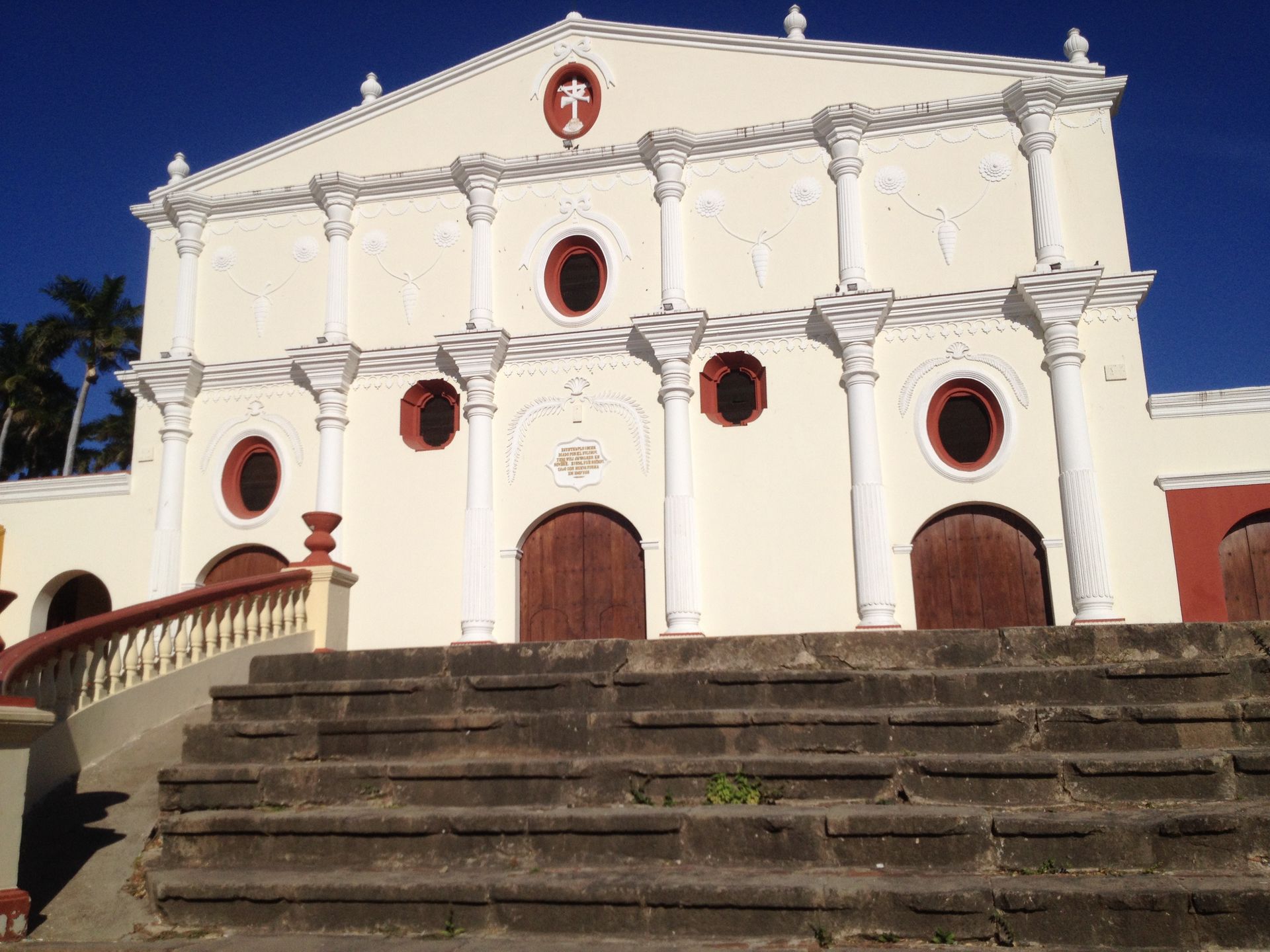 White church building with brown doors and steps leading up; blue sky.