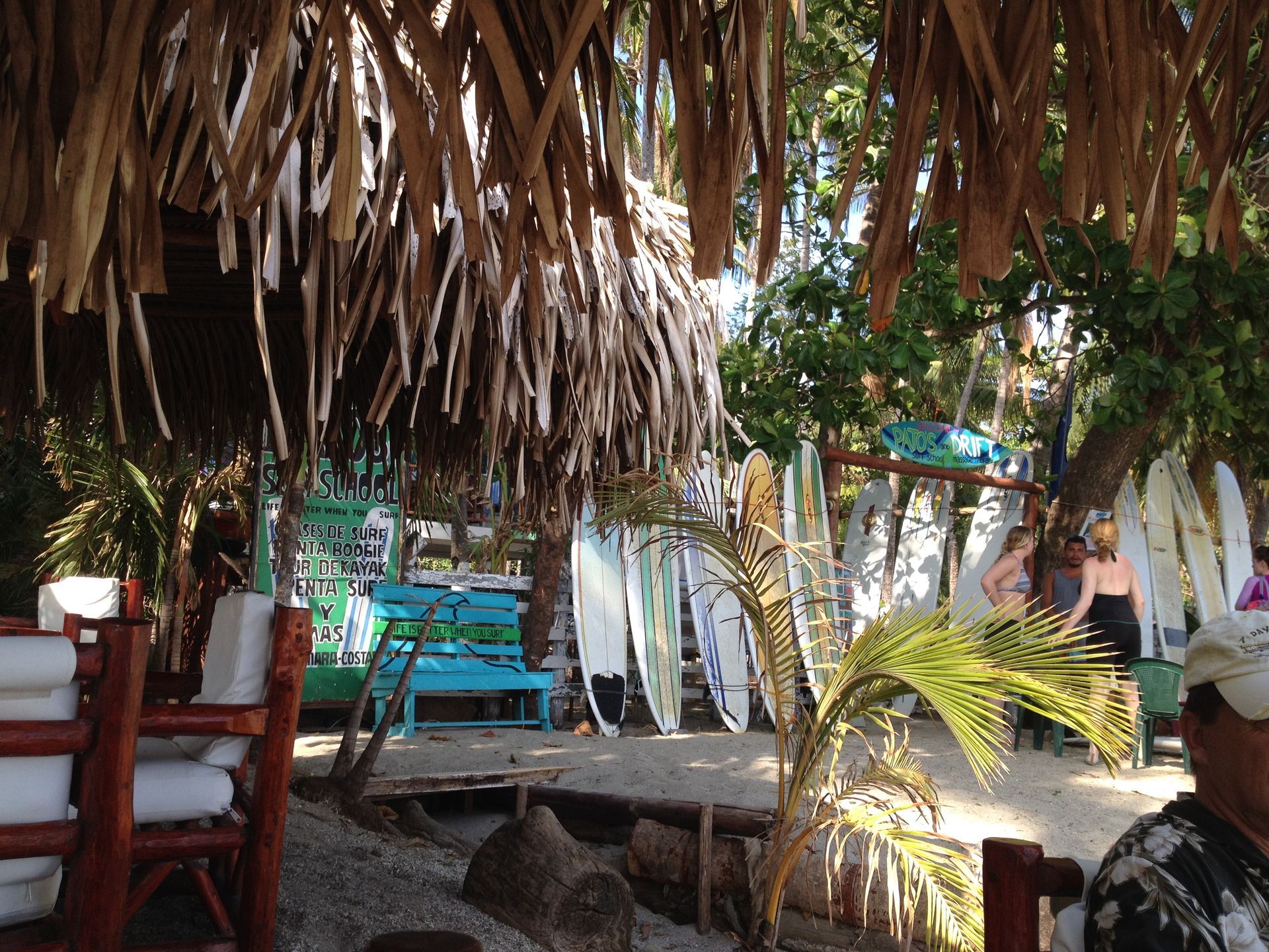 Beachside surf shop with thatched roof, surfboards, and people.