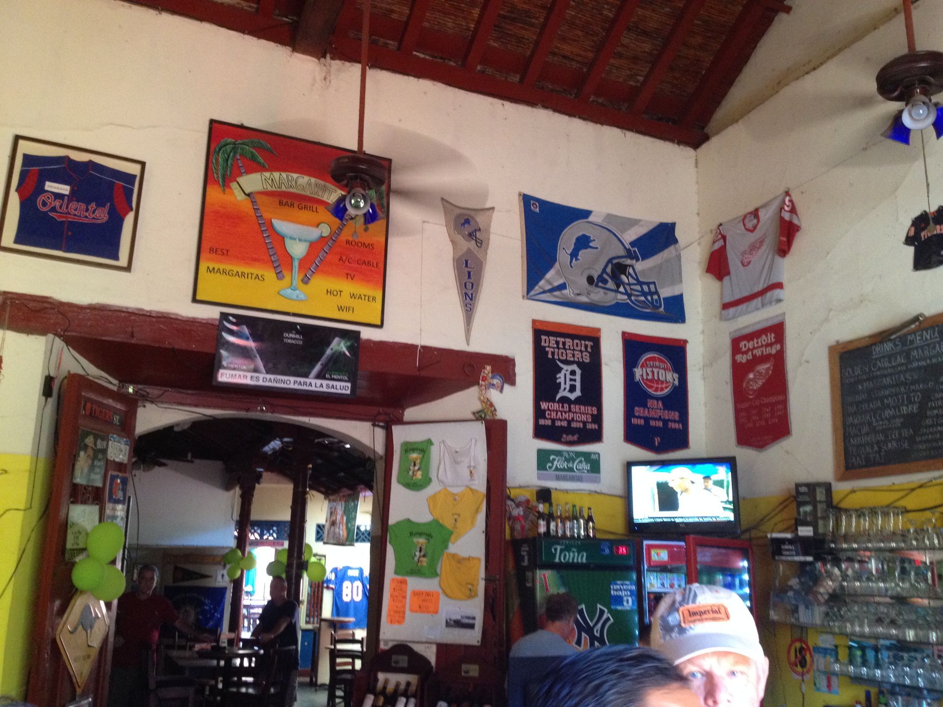 Interior of a sports bar decorated with sports team flags and televisions; people and drinks visible.