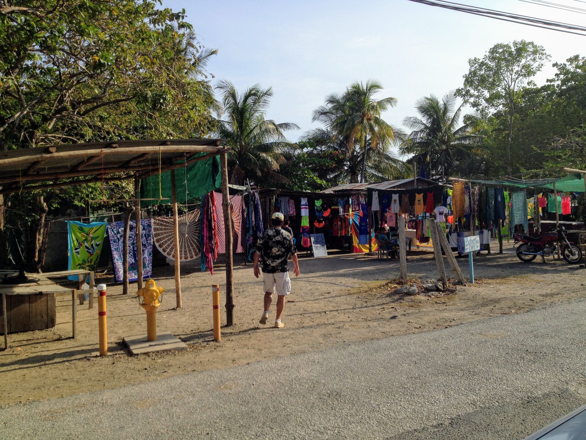 Man walking toward beachside souvenir stalls with colorful clothing on display.