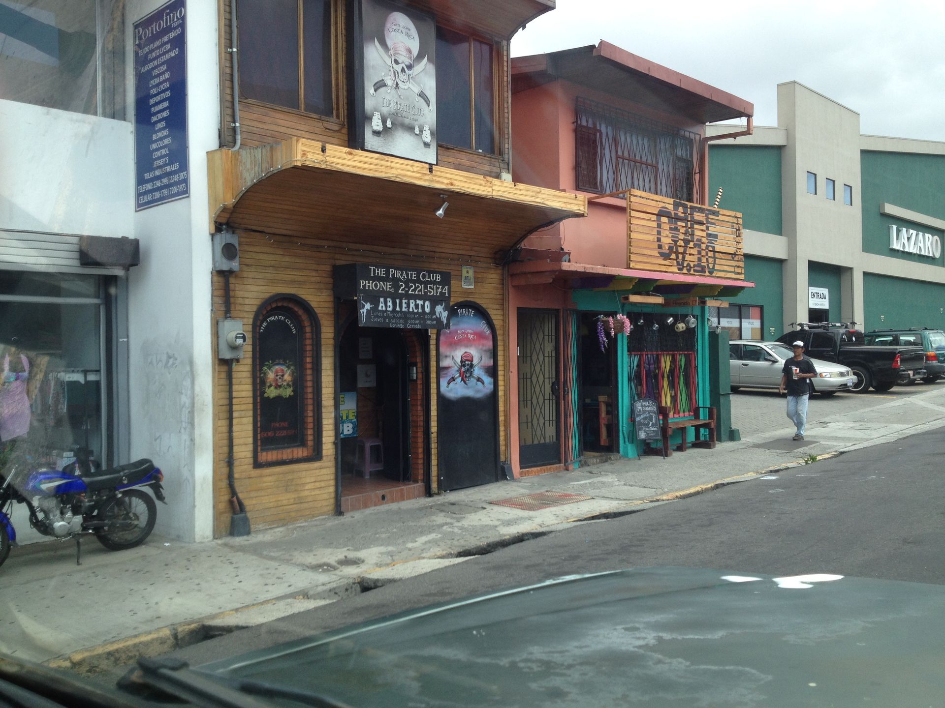 Street view of shops: motorcycle, wooden facade, colorful signage, person walking.