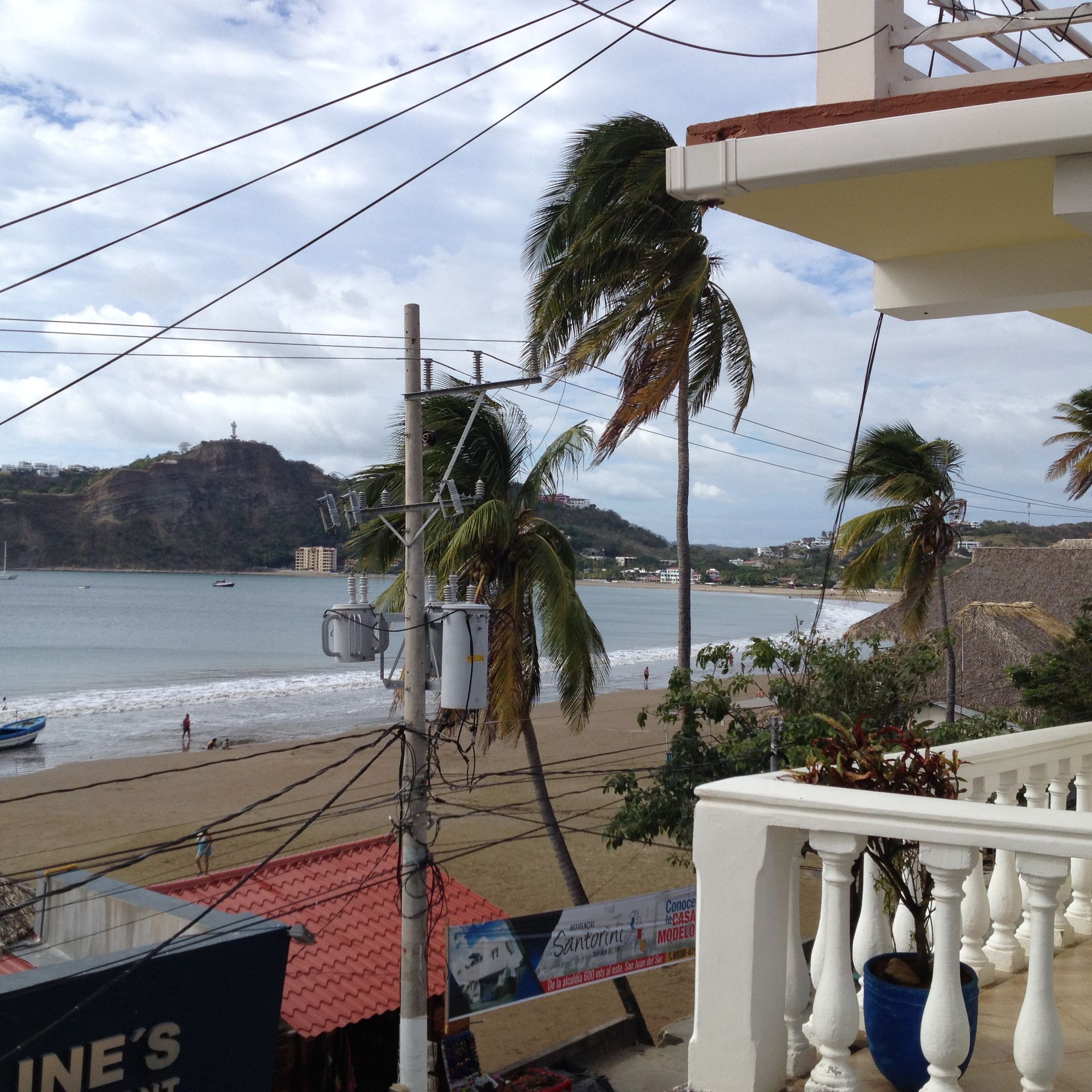 Beach scene with palm trees, sandy shore, ocean, and a building with a balcony.