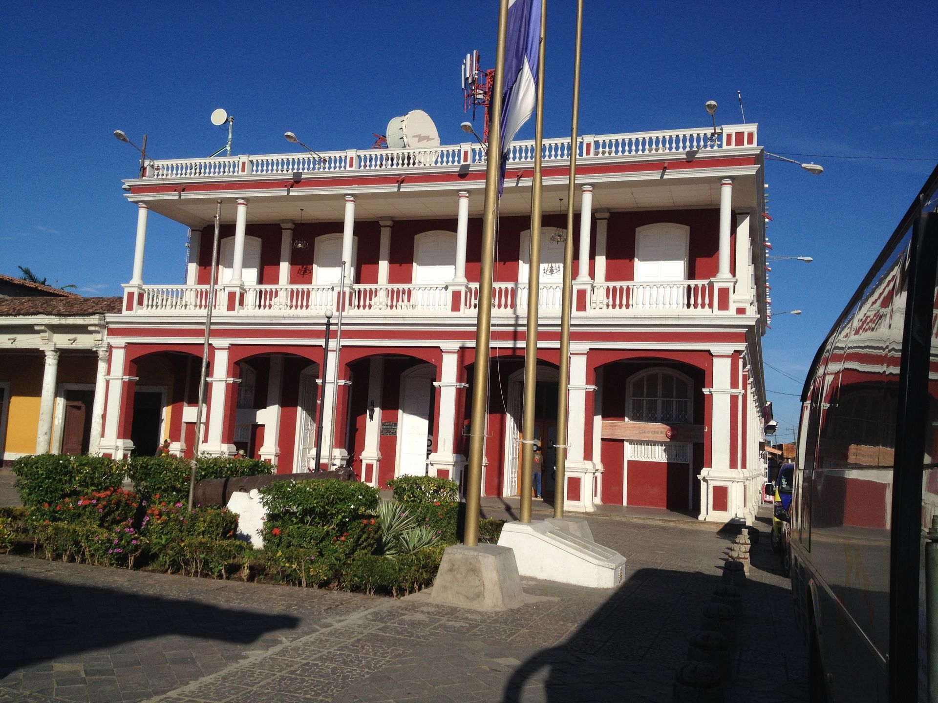 Two-story red and white building with balcony and flags, possibly a government building in a sunny outdoor setting.