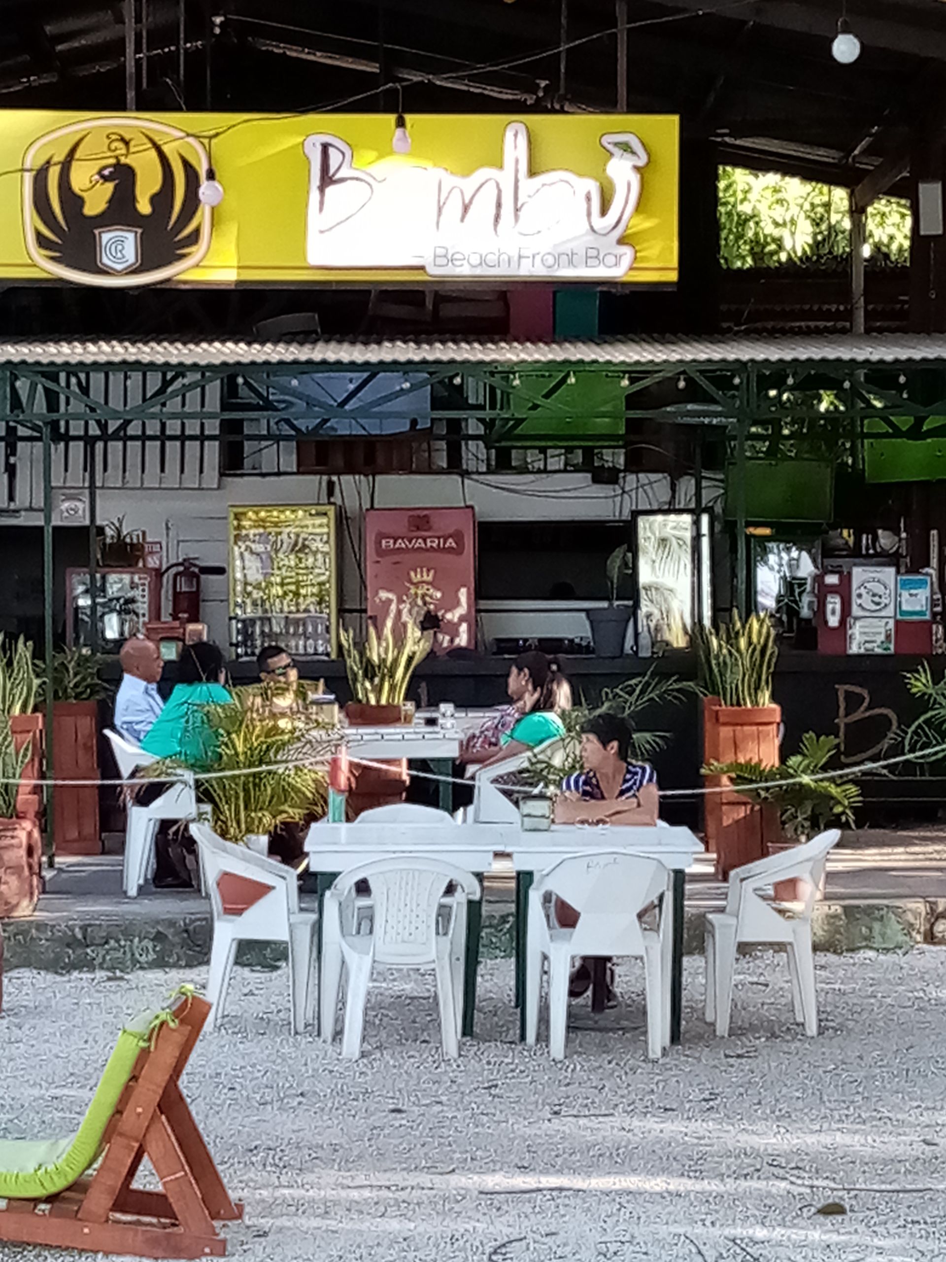 Restaurant patio with white tables, seated people, and sign that reads 