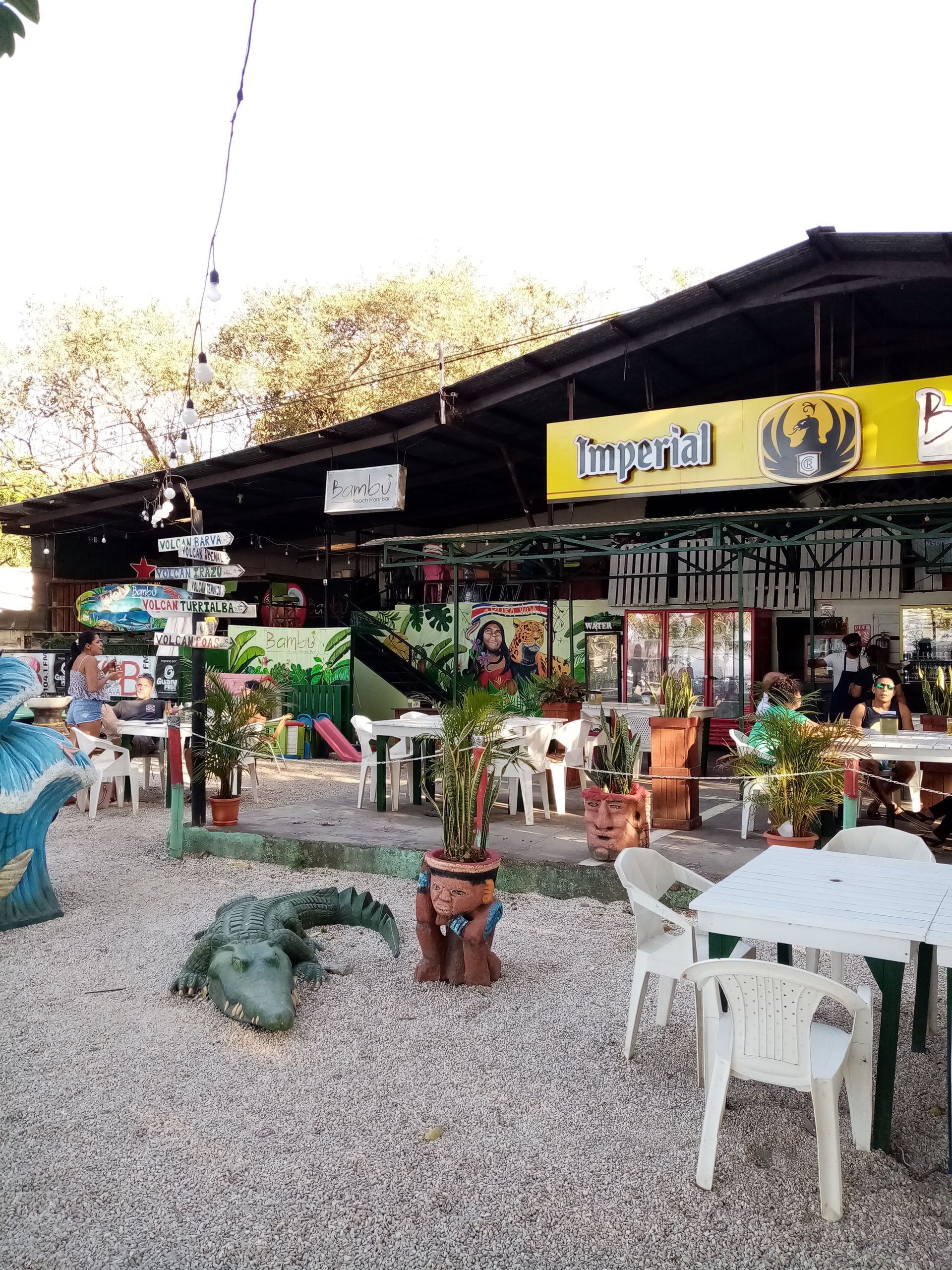 Outdoor restaurant with tables, decorative plants, and a crocodile statue. 