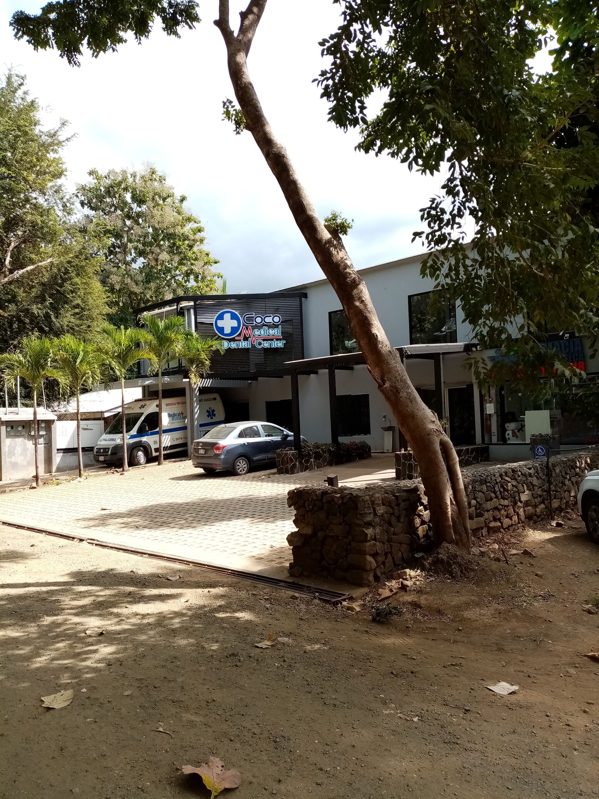 A two-story building with a sign and parked cars. A tree grows in front of the building.
