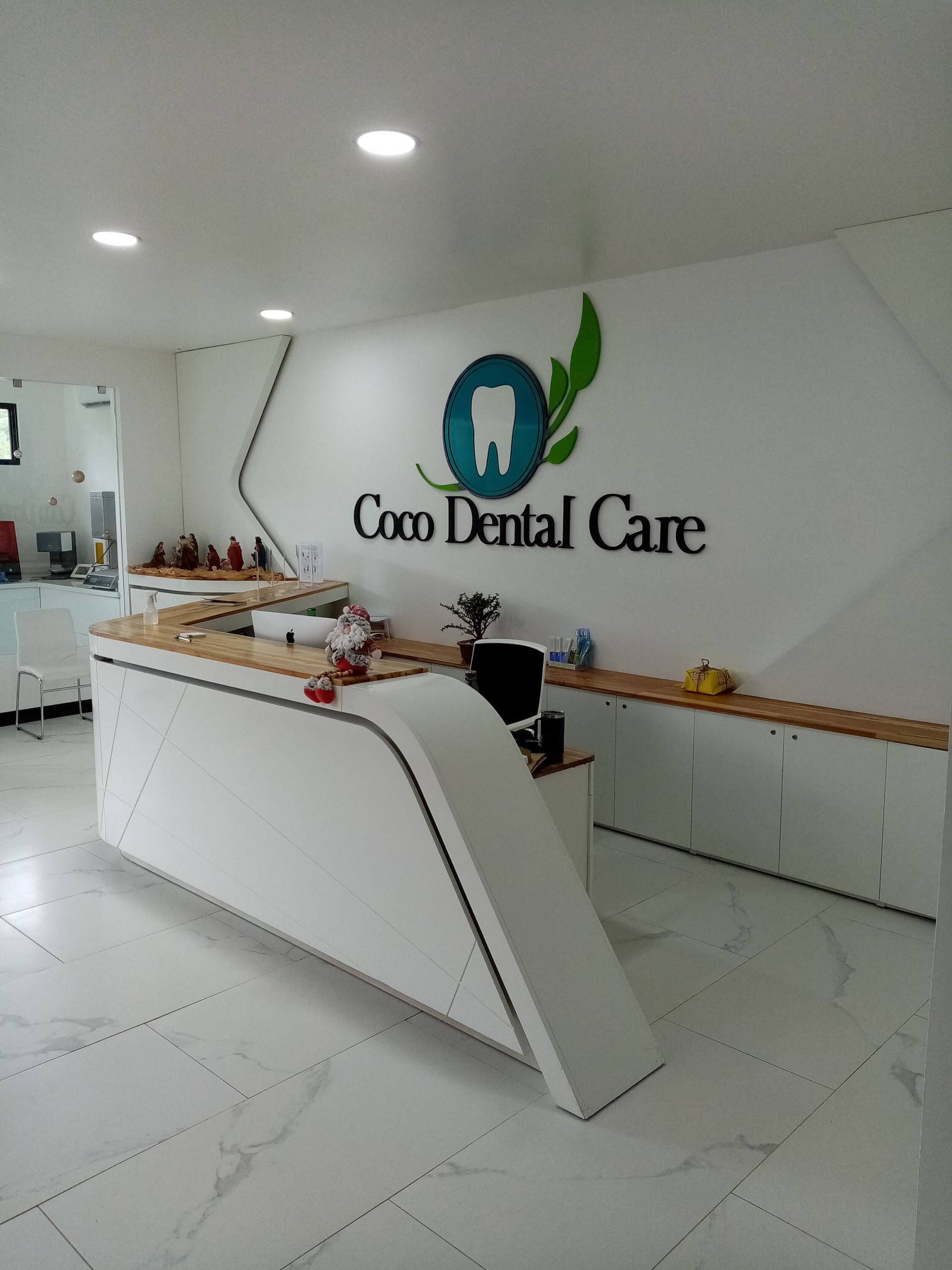 Interior of Coco Dental Care reception area with white desk, logo on wall.