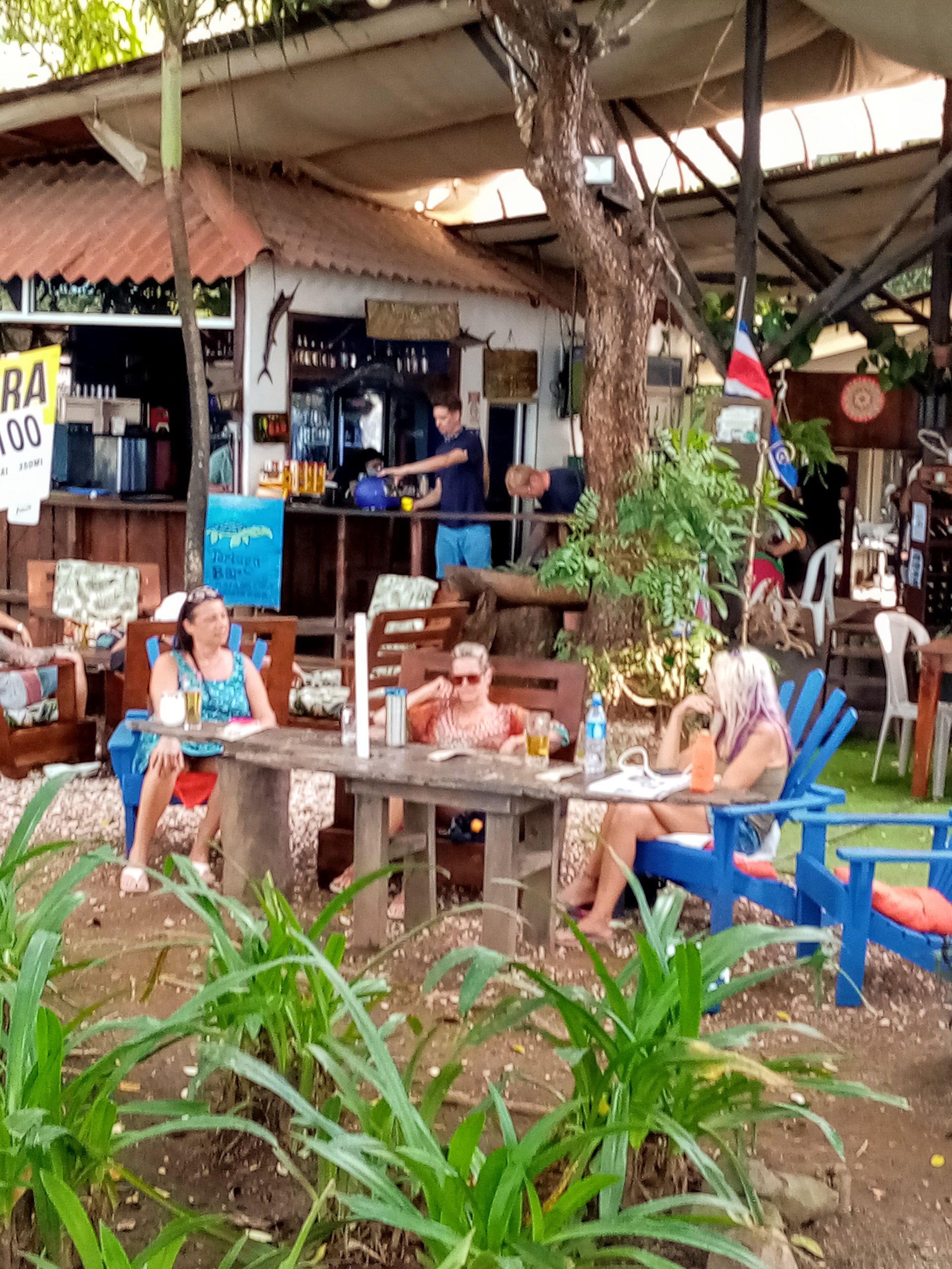 People at outdoor bar with drinks, Costa Rica flag, and bar in the background.