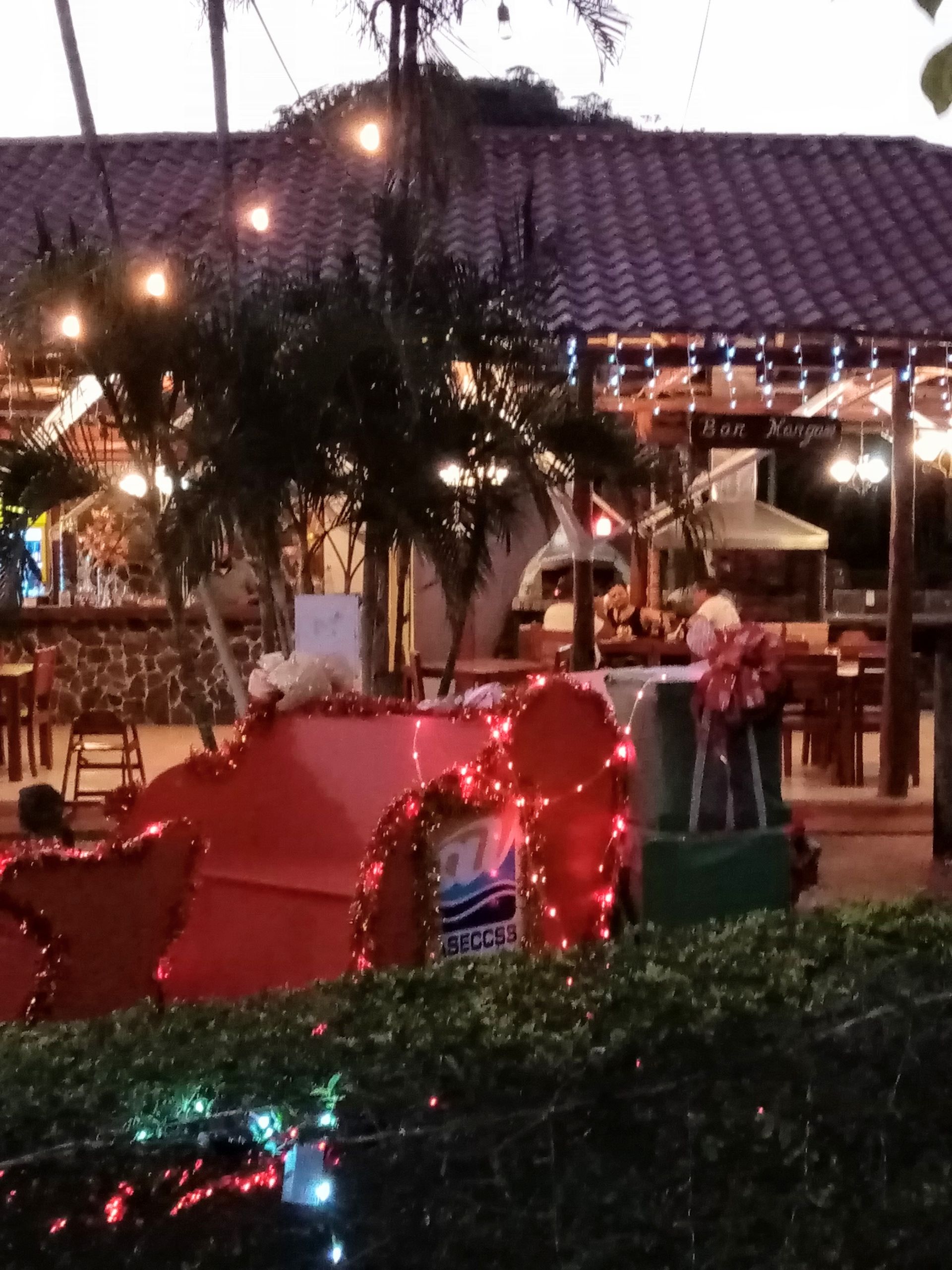Red decorative cart with lights in front of a restaurant at dusk, with outdoor seating and string lights.