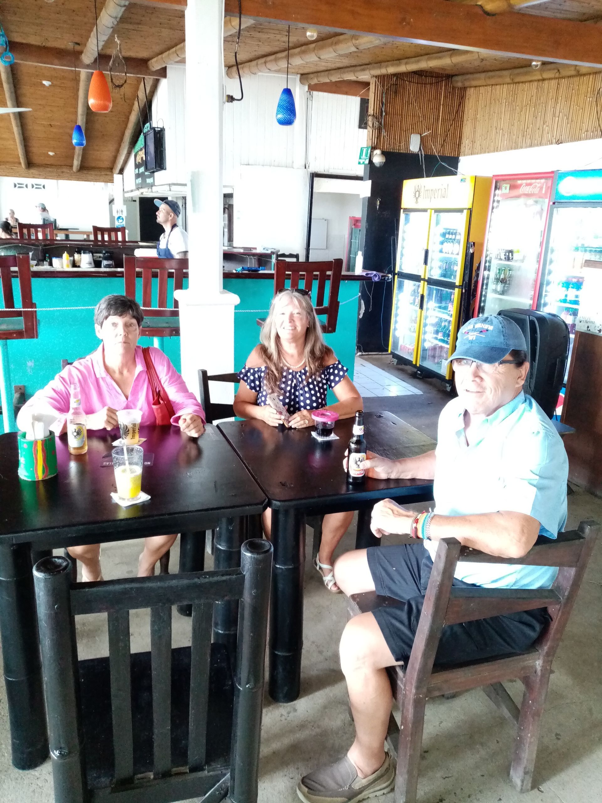 Three people seated at a table in a bar; two women, one man, drinks on the table.