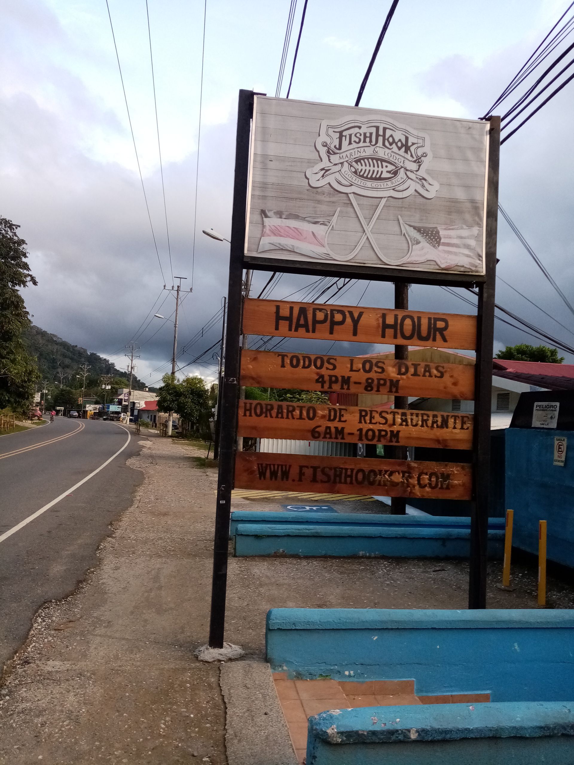 Wooden sign for Happy Hour by a road. Reads 