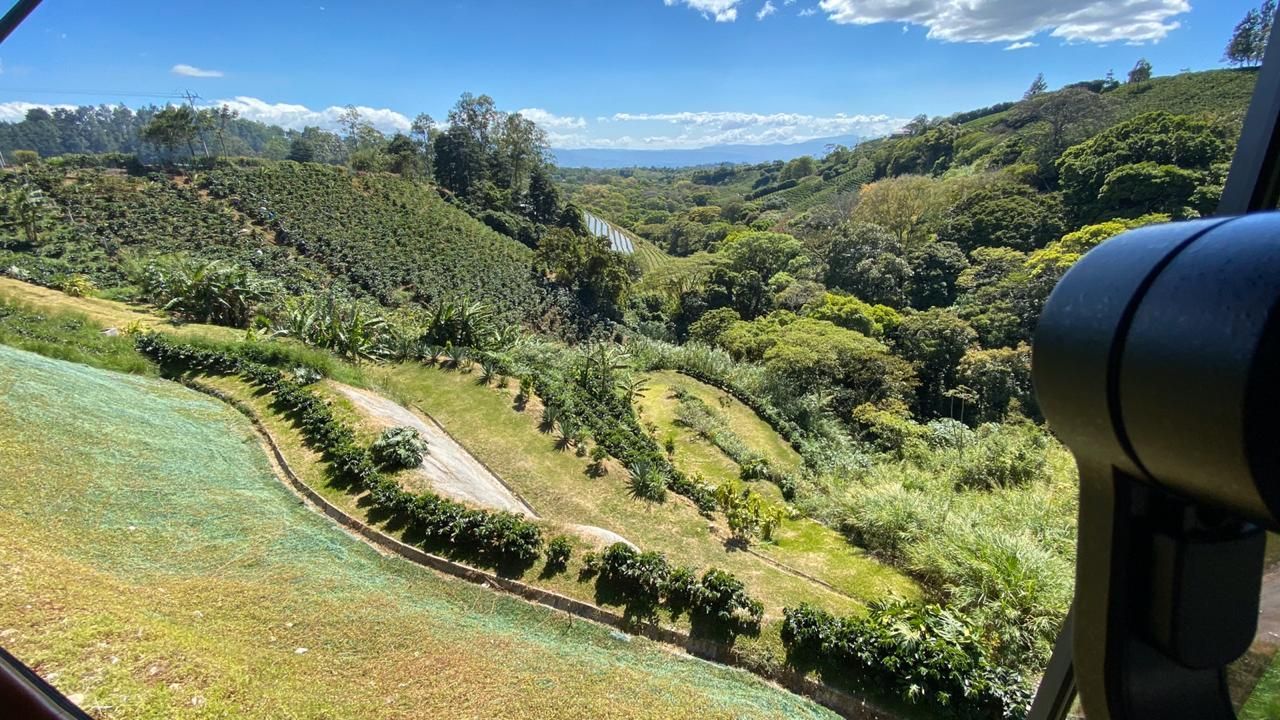 Green hillside with terraced farmland, overlooking a valley under a blue sky, camera lens in the right corner.