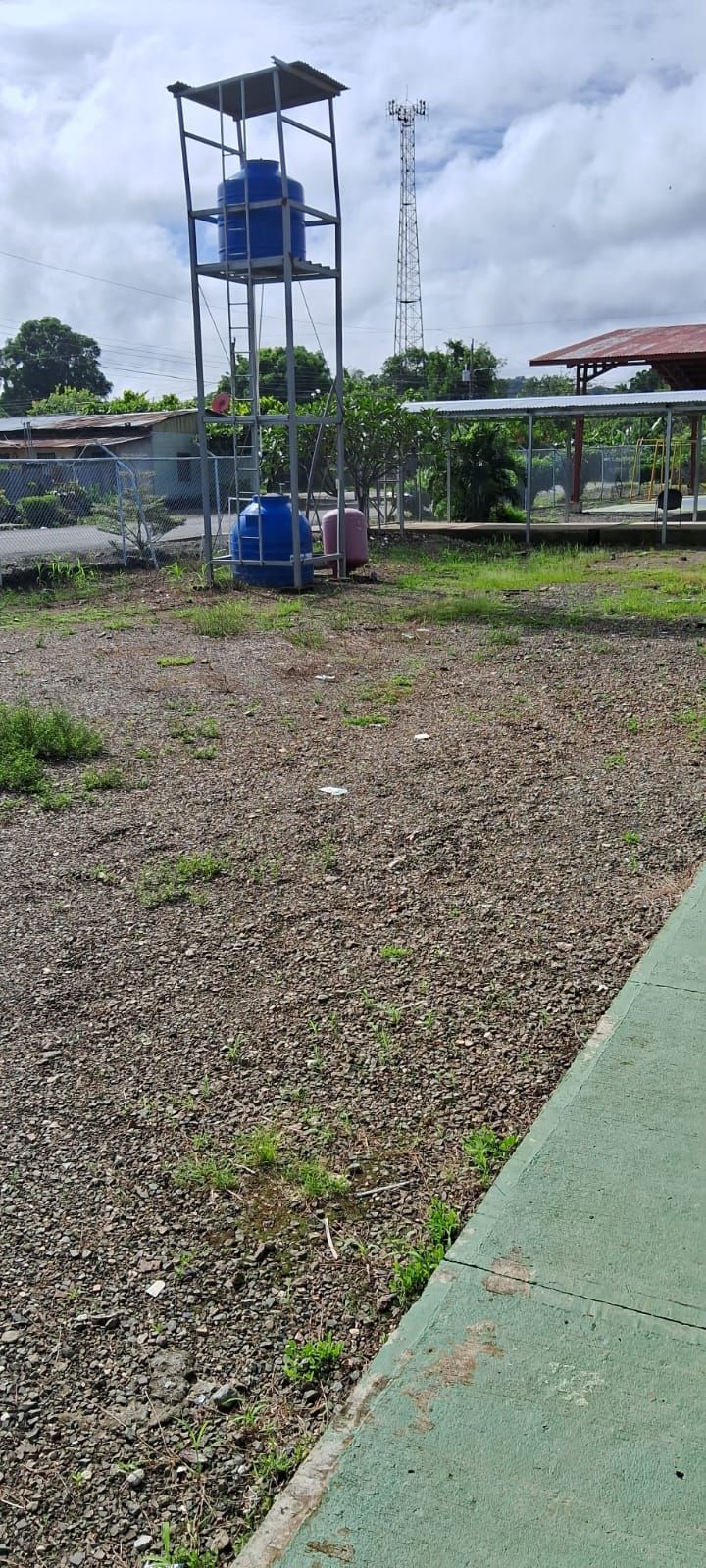 Water tanks on a metal structure, gravel ground, and a cloudy sky.