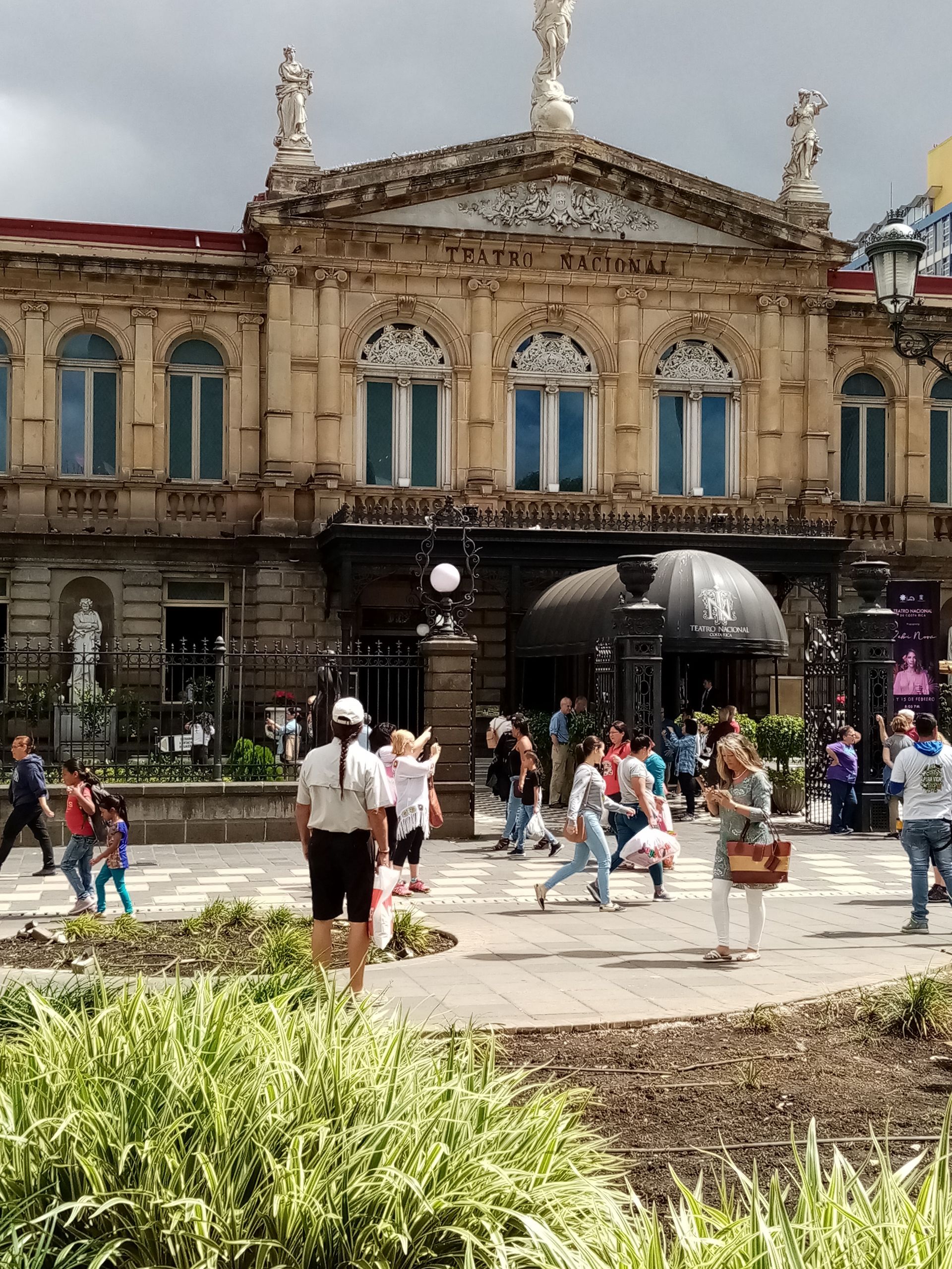 Ornate building with people walking in front; cloudy sky.