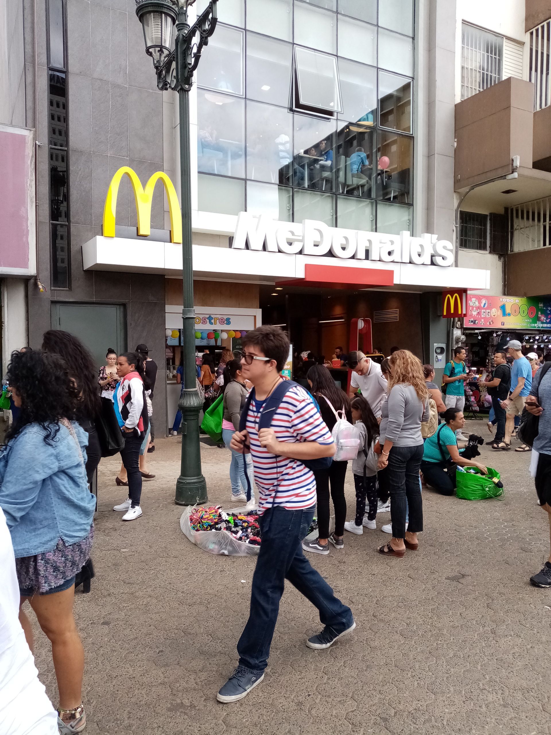 McDonald's exterior with a crowd of people. Yellow arches, white sign, glass windows, and a street scene.