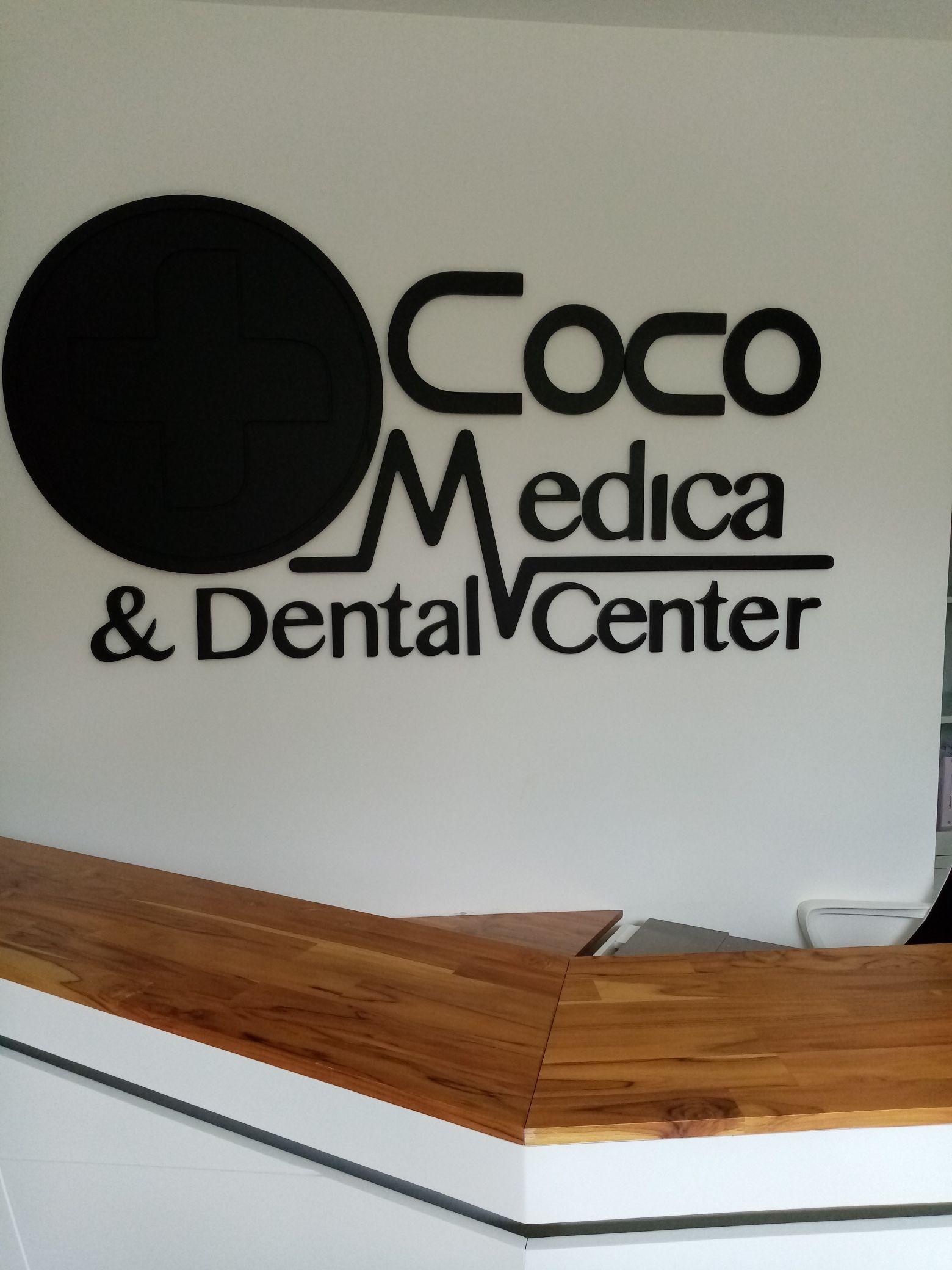 Coco Medica & Dental Center sign above a reception desk. Black circle and text on a white wall.