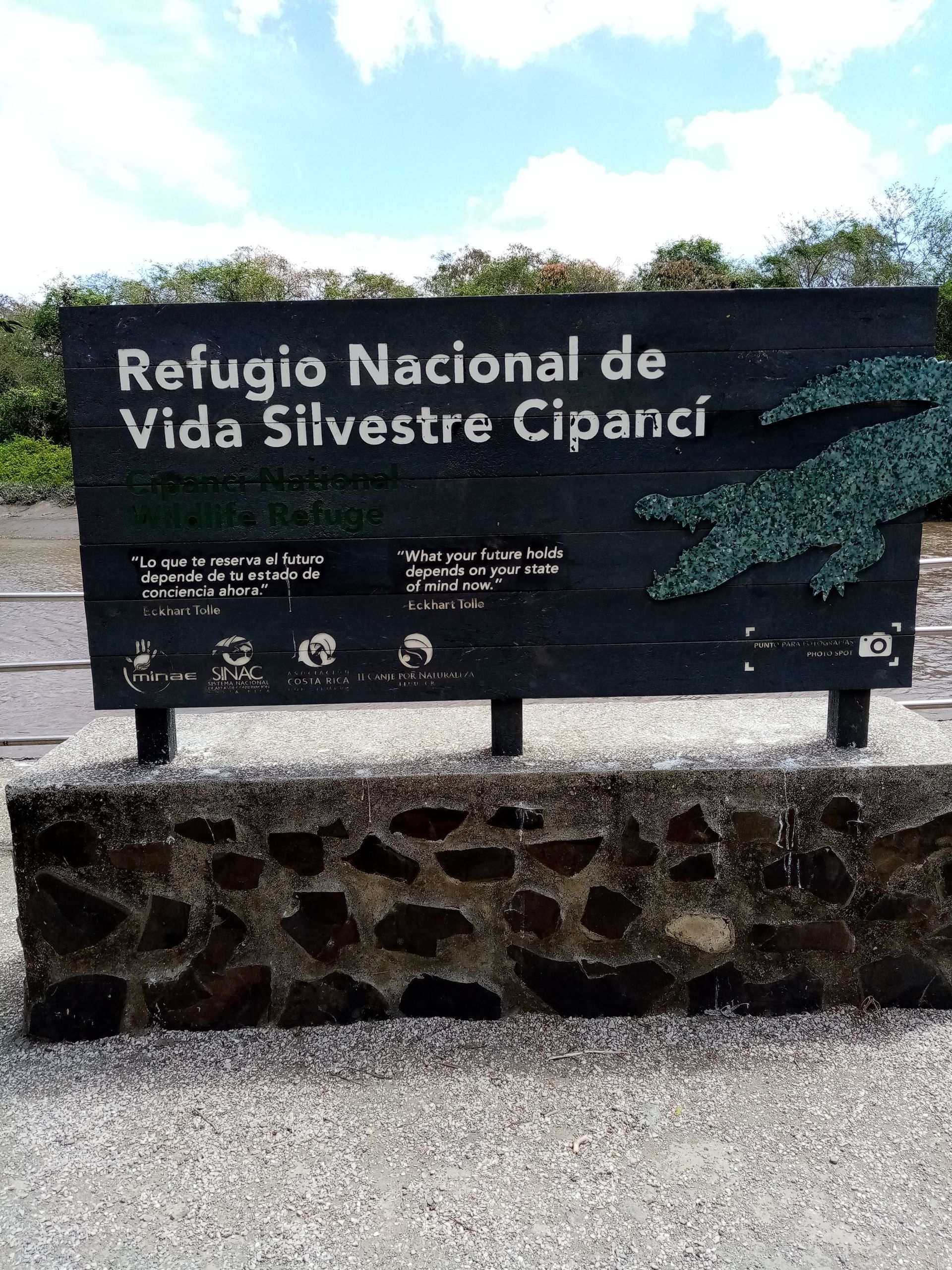 Sign for Refugio Nacional de Vida Silvestre Cipancí, in Spanish, on a dark wooden board, on a stone base, outdoors.