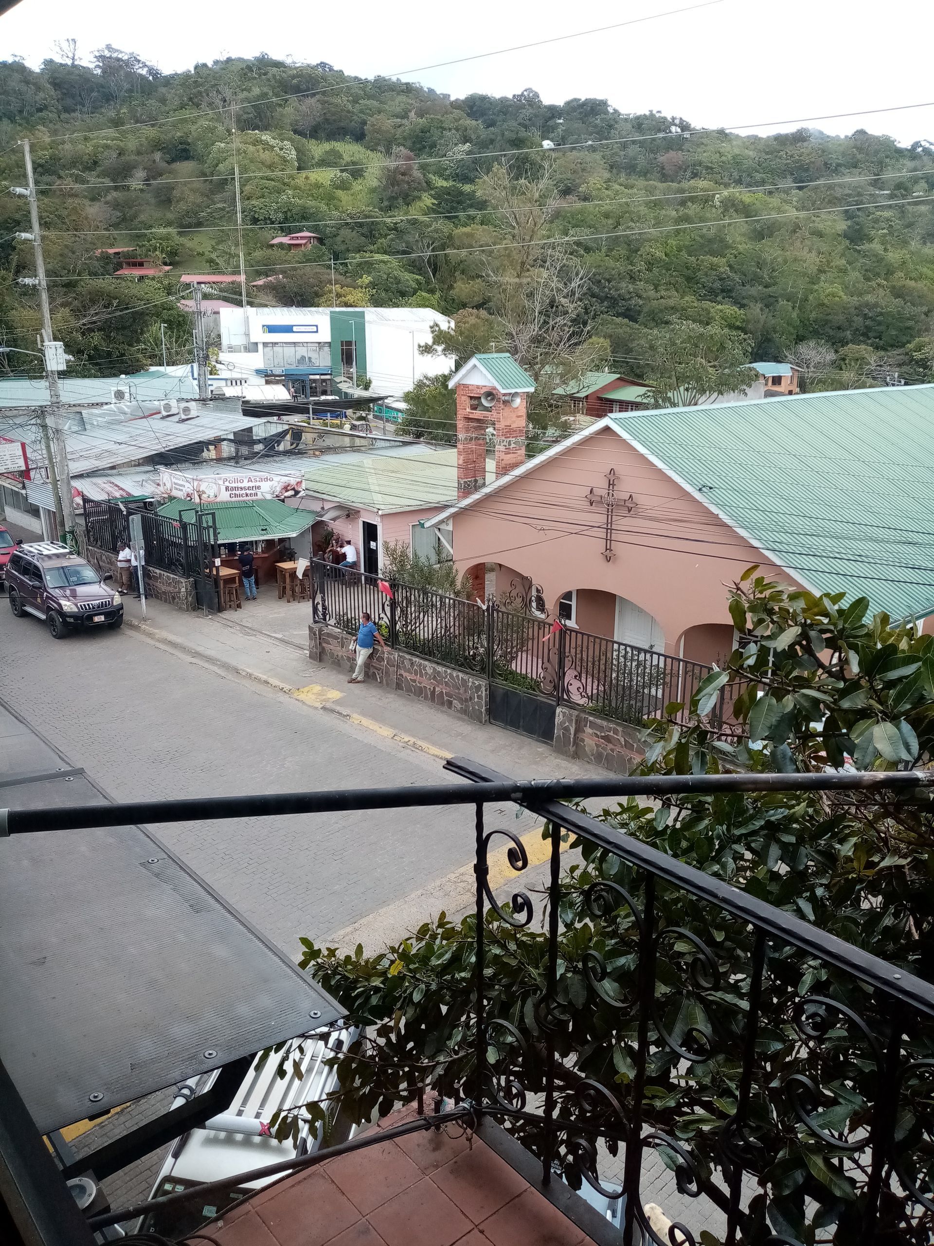 Street scene in a mountain town with buildings, vehicles, and a church. Lush green trees in the background.