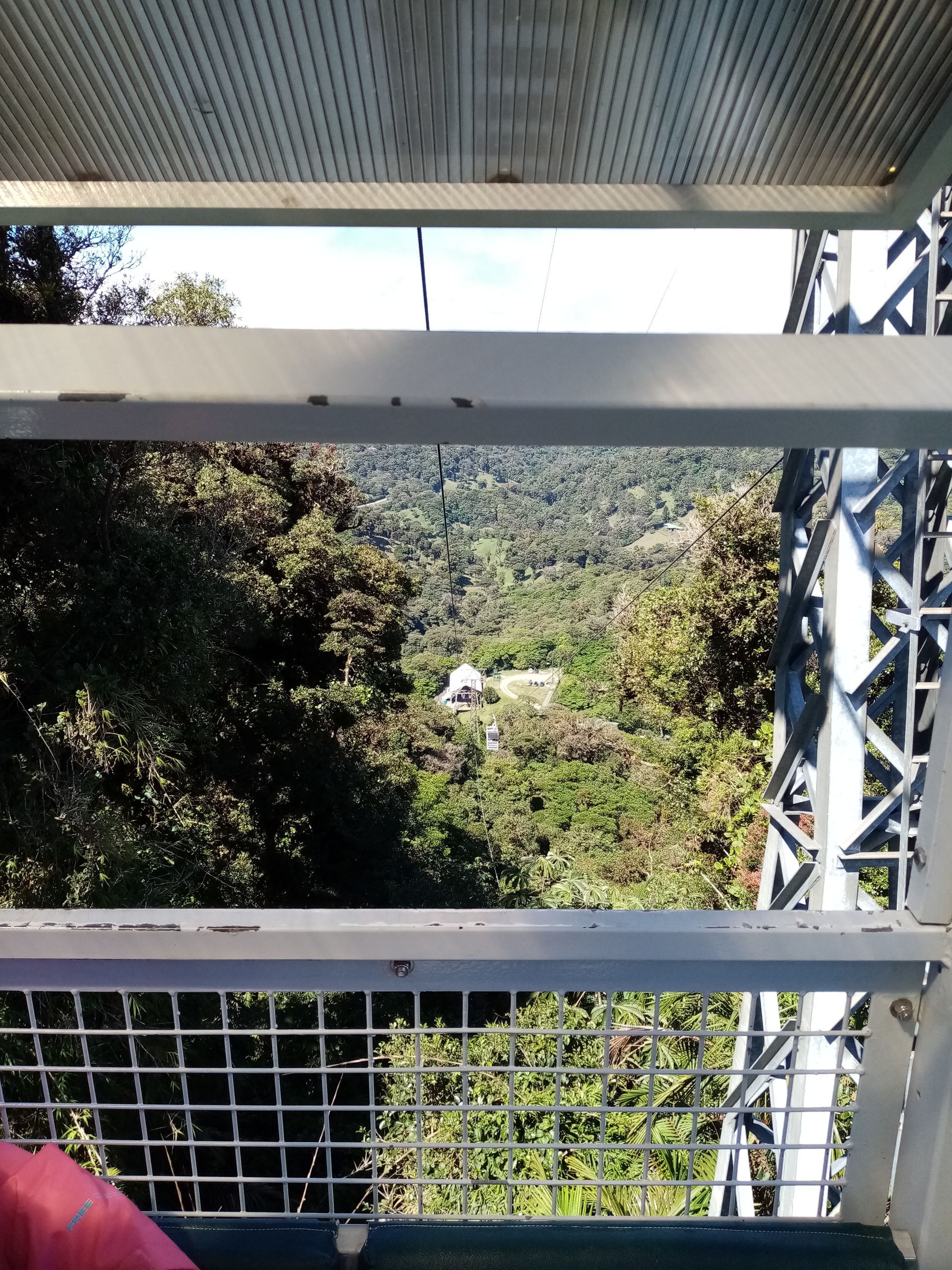 View from a metal structure overlooking a lush green valley with a small building.