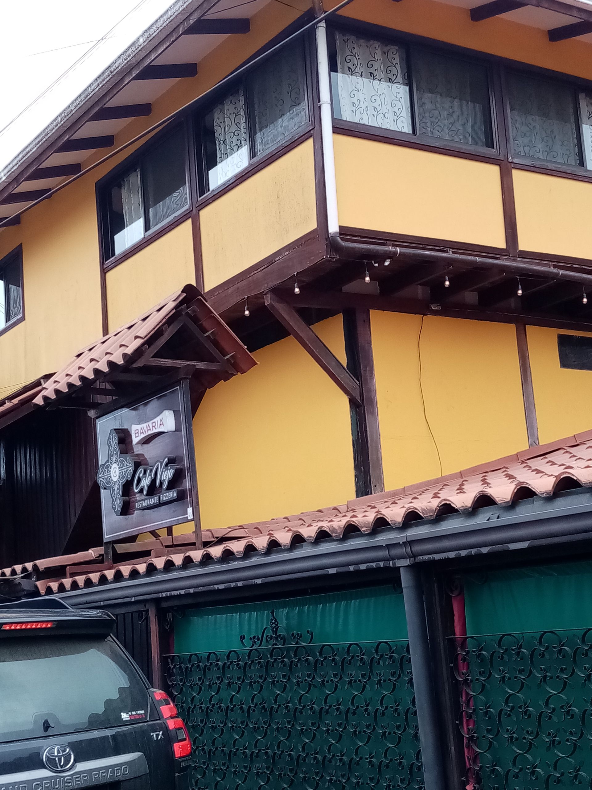 Yellow building with brown trim and red tile roof; a sign hangs below a small covered entrance.