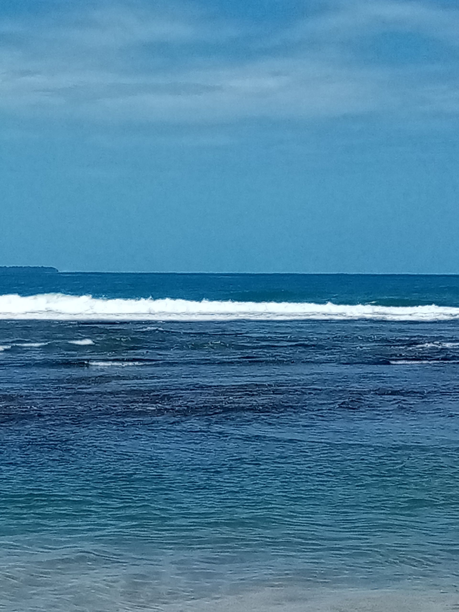 Blue ocean with white waves under a clear blue sky.