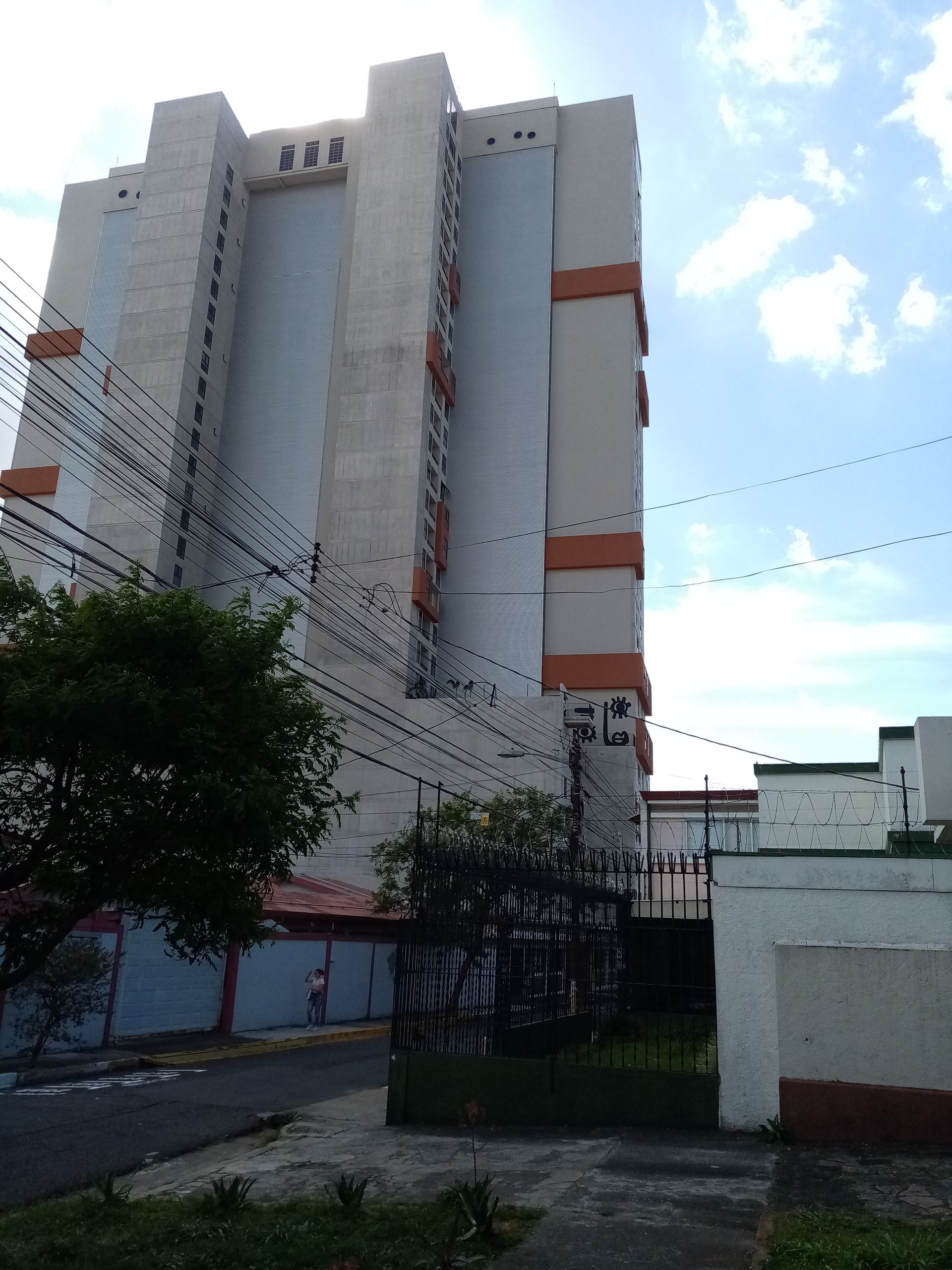 Tall concrete building with orange trim against a blue sky, power lines in view.