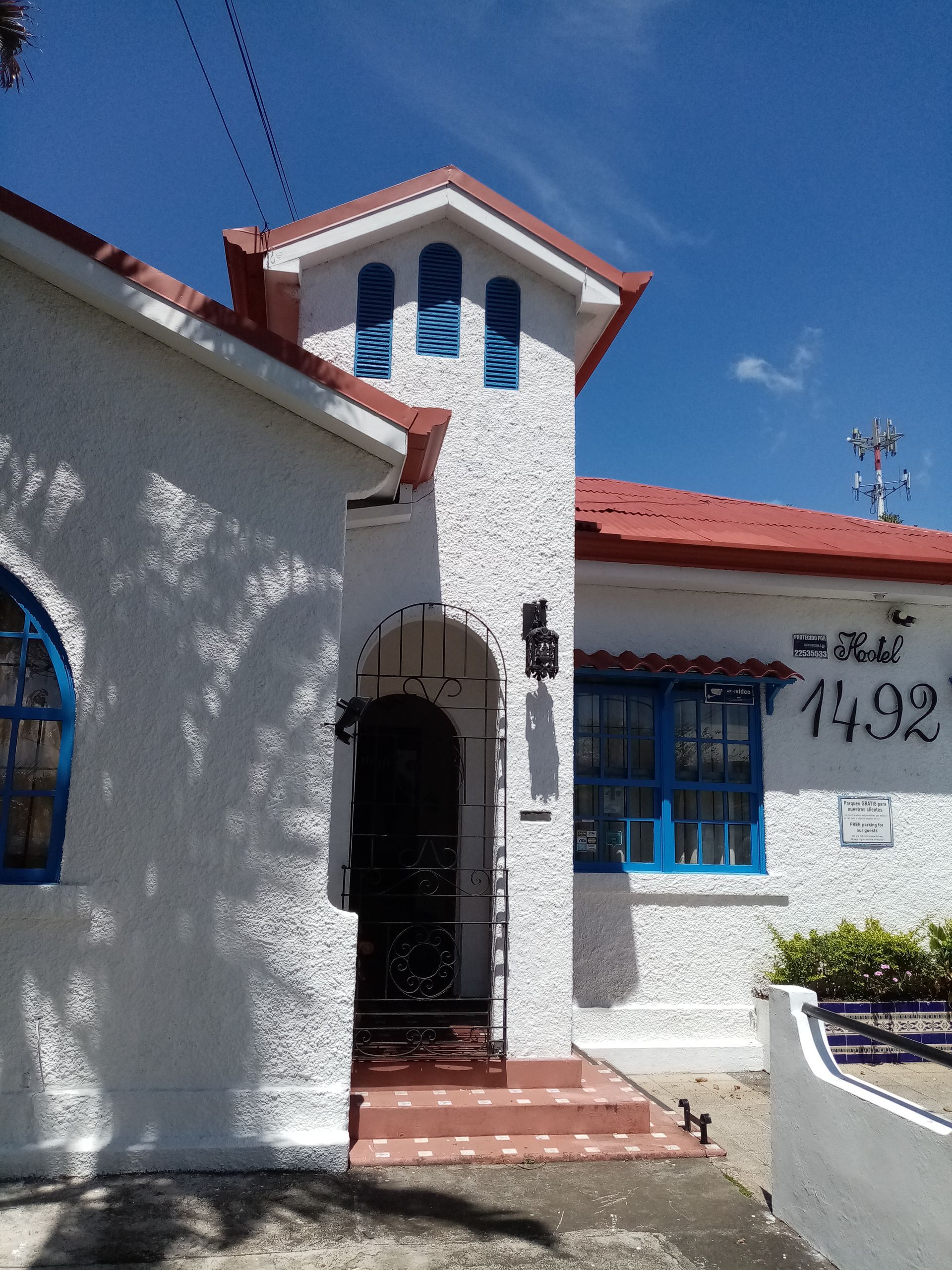 White stucco building with red roof, blue window frames, and arched entryway.