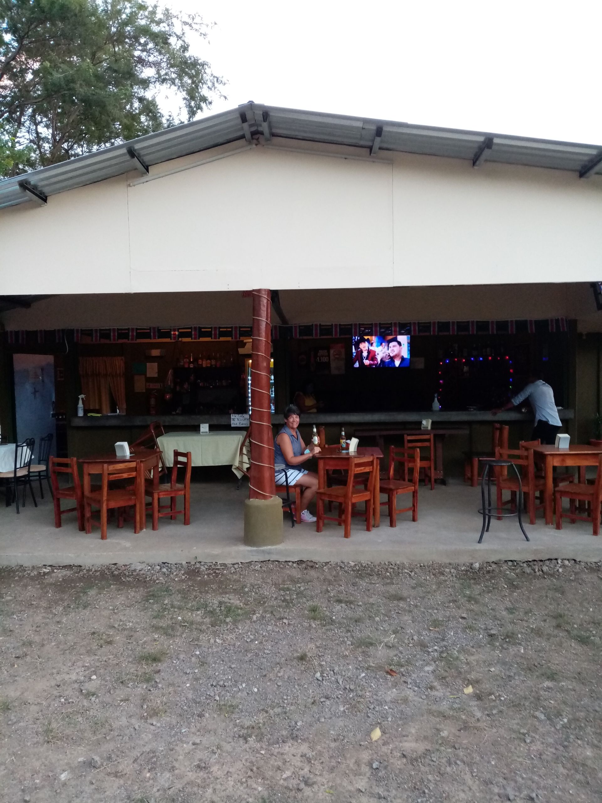 Outdoor bar with wooden tables and chairs; person seated at table.