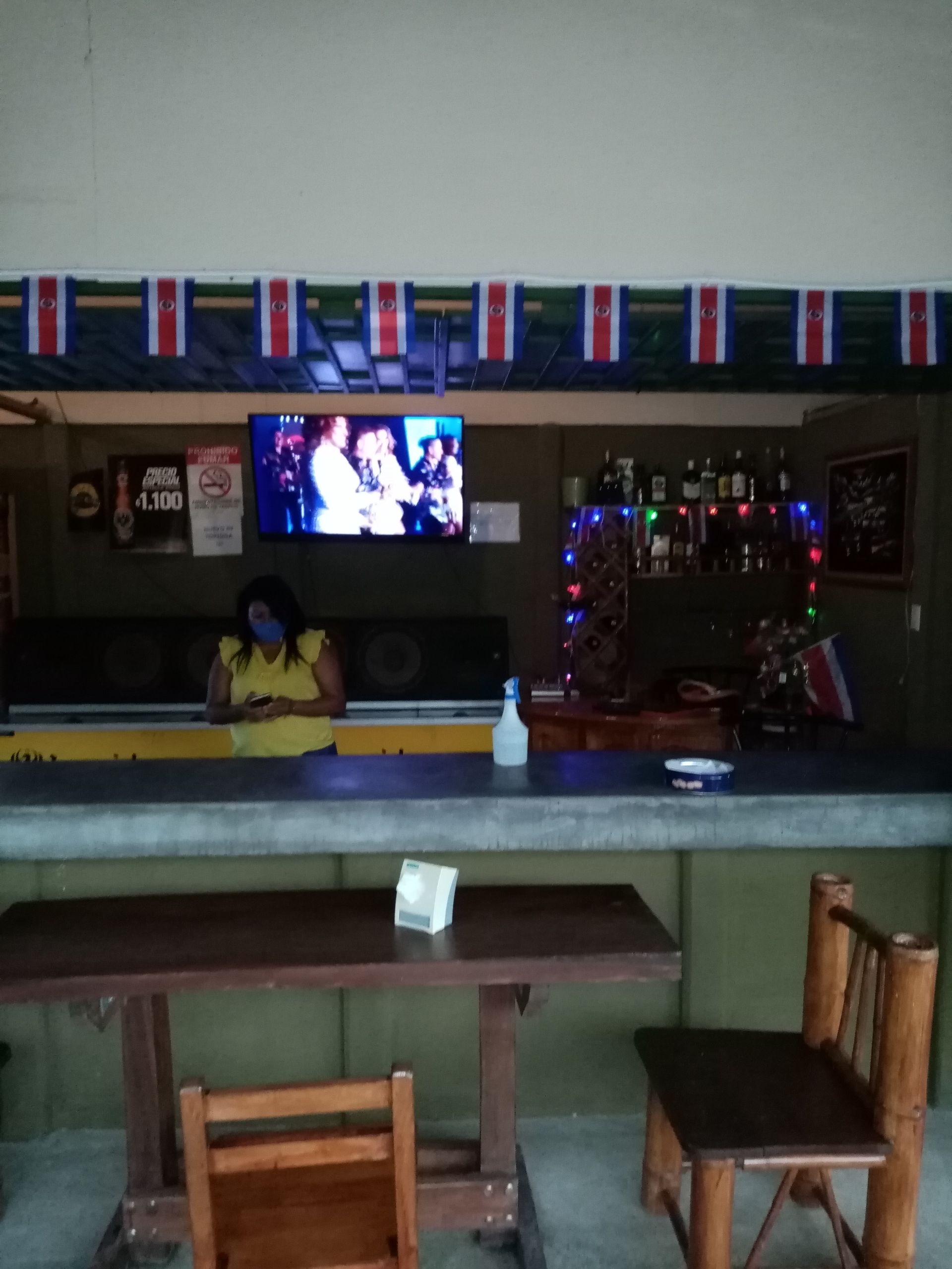 A bar with a person behind the counter. A TV is on, decorations and Costa Rican flags are visible.