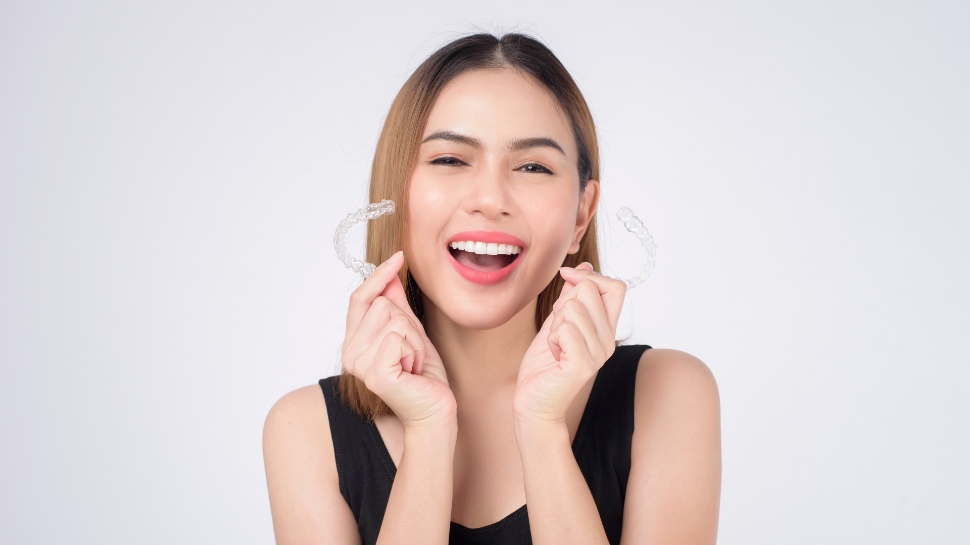Woman holding clear aligners, smiling.