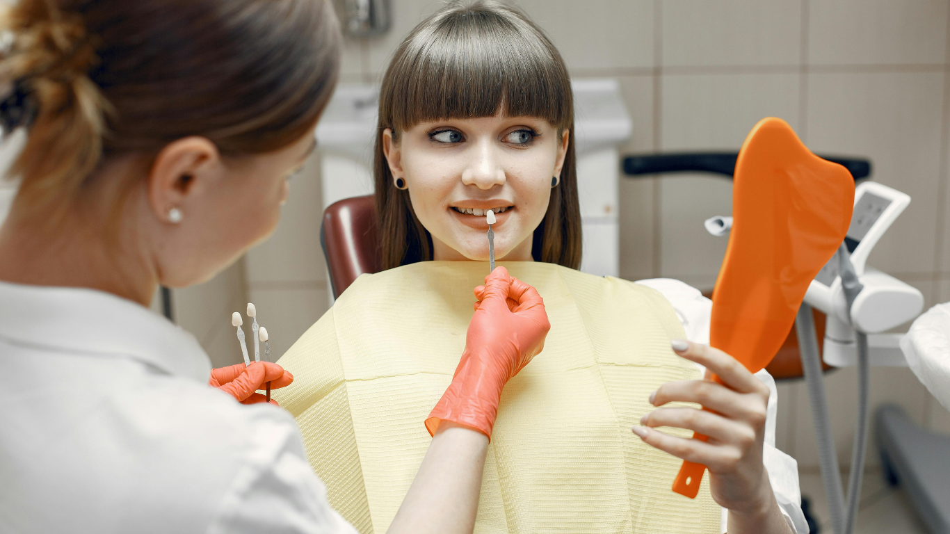 Dentist examining a patient holding an orange dental model in a clinic