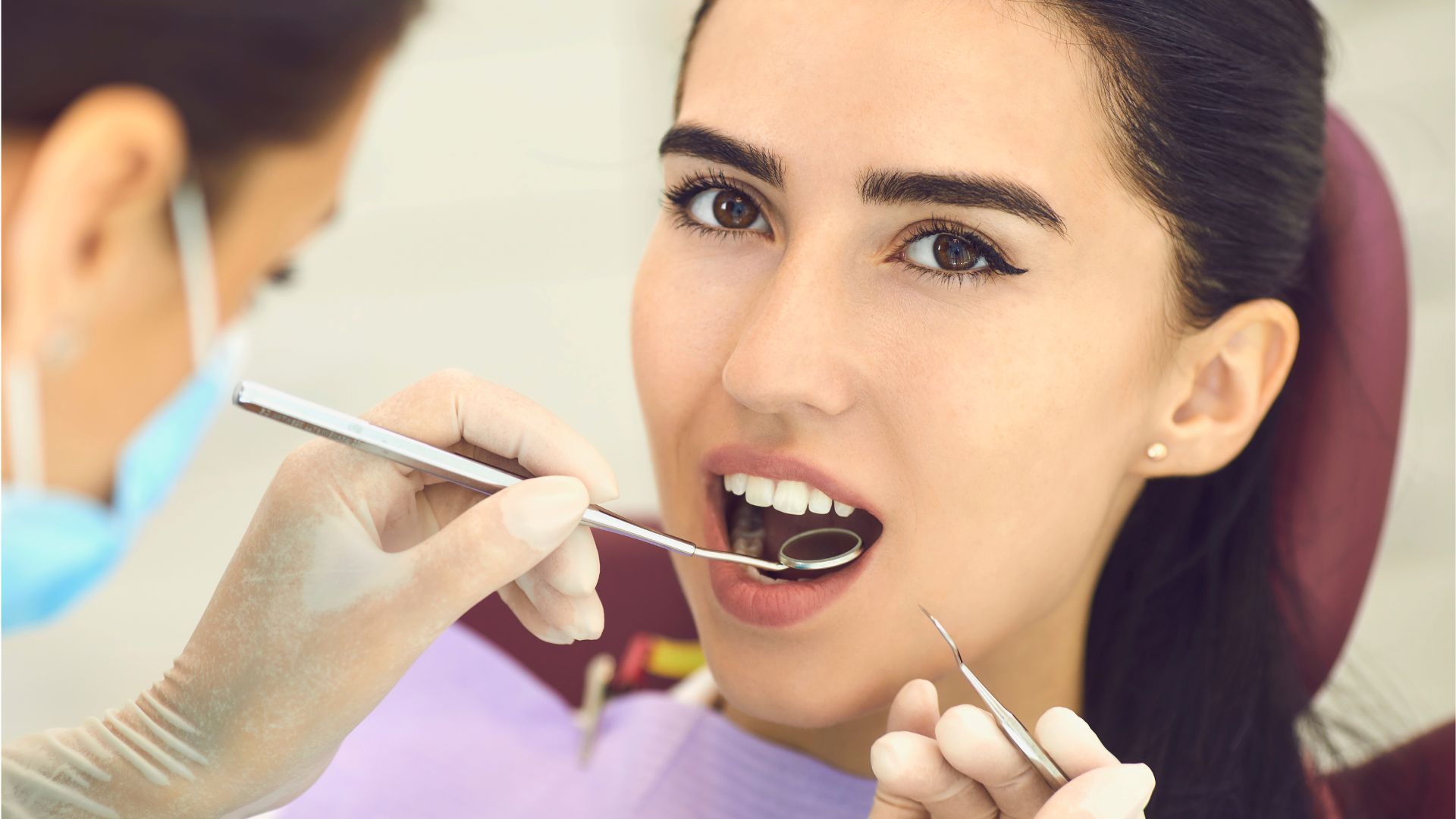 Dentist examining a smiling patient’s teeth with dental mirror and tools in a clinic