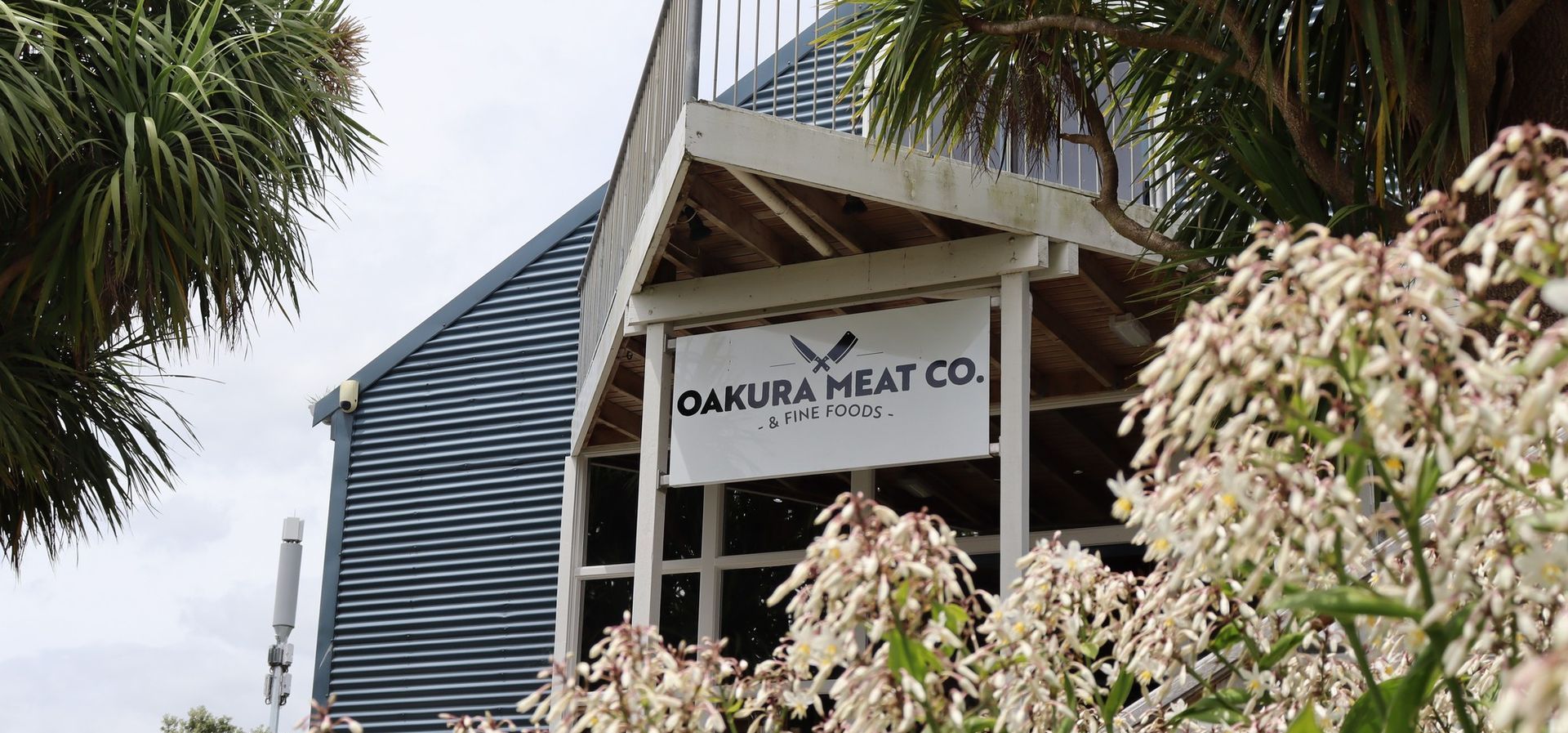 A building with a sign that says `` sakura meat co. '' is surrounded by flowers.