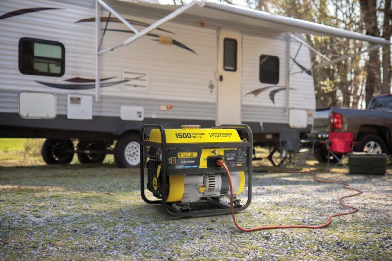 Yellow generator running beside a beige RV at a campsite, with a truck in the background.